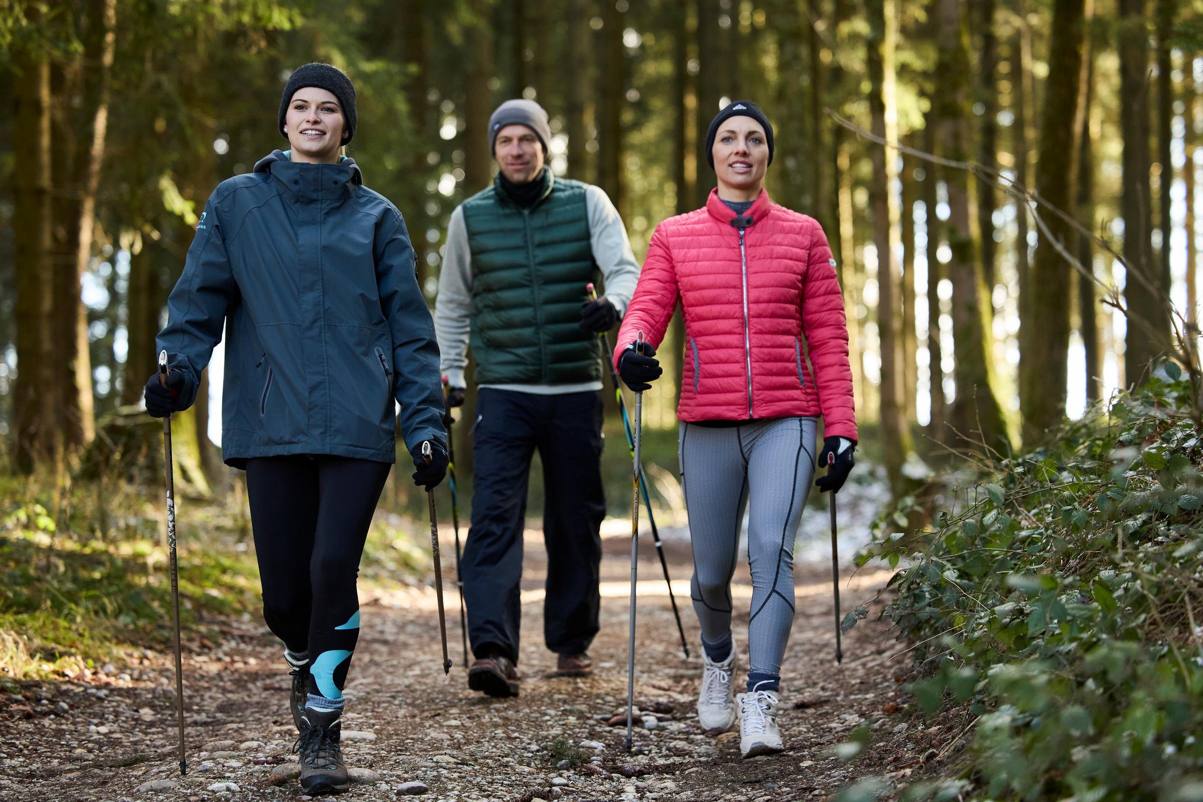Drei Menschen beim Wandern in einem Wald, alle tragen wetterfeste Kleidung und Wandernadeln