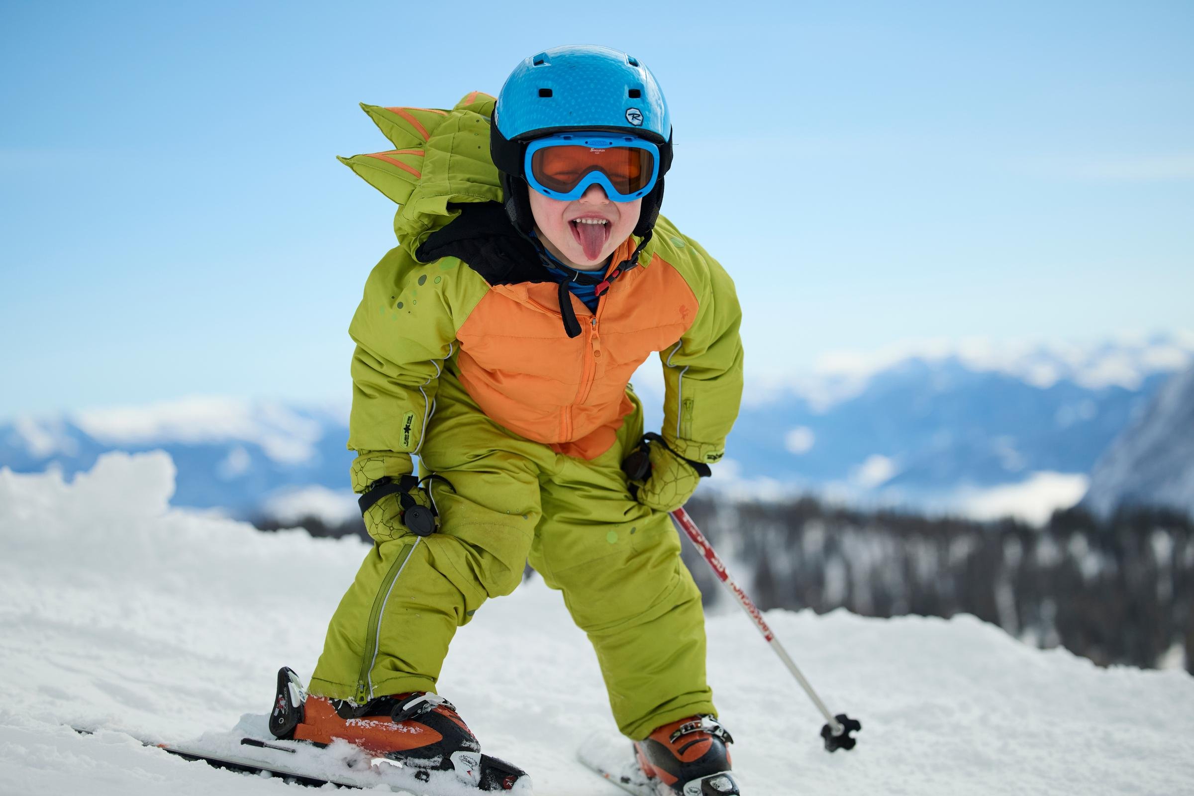 Kinderskifahrer in Skibrille und Helm auf schneebedecktem Berg in Alpenlandschaft