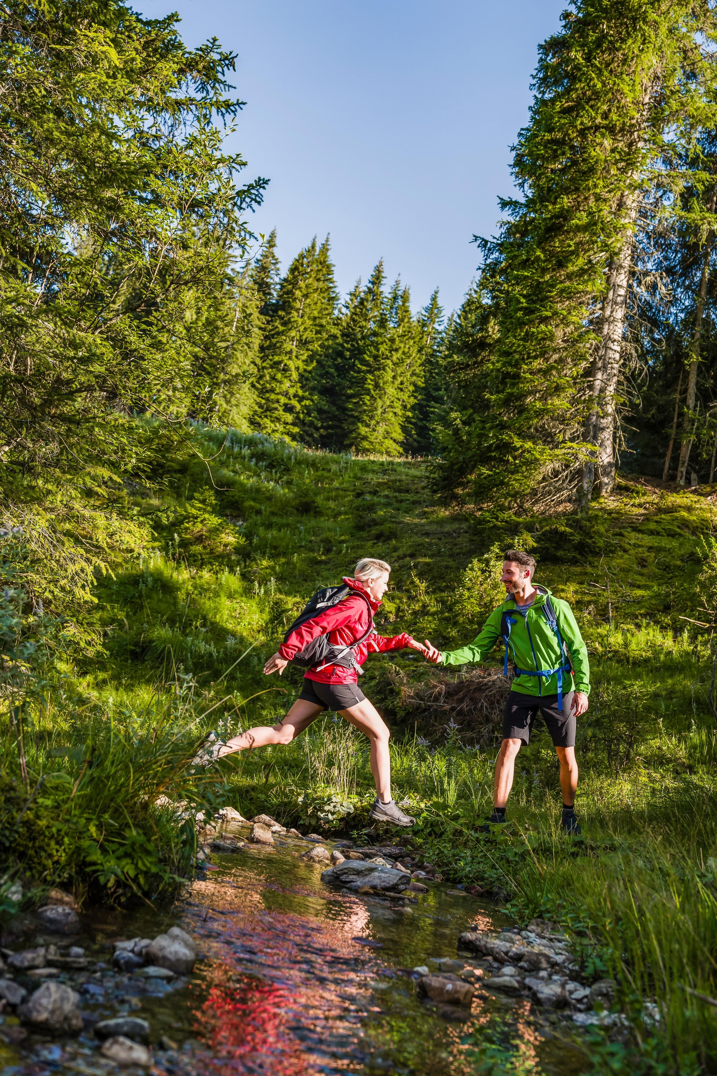 Zwei Kinder beim Wandern entlang eines Flusses in einer grünen Waldlandschaft