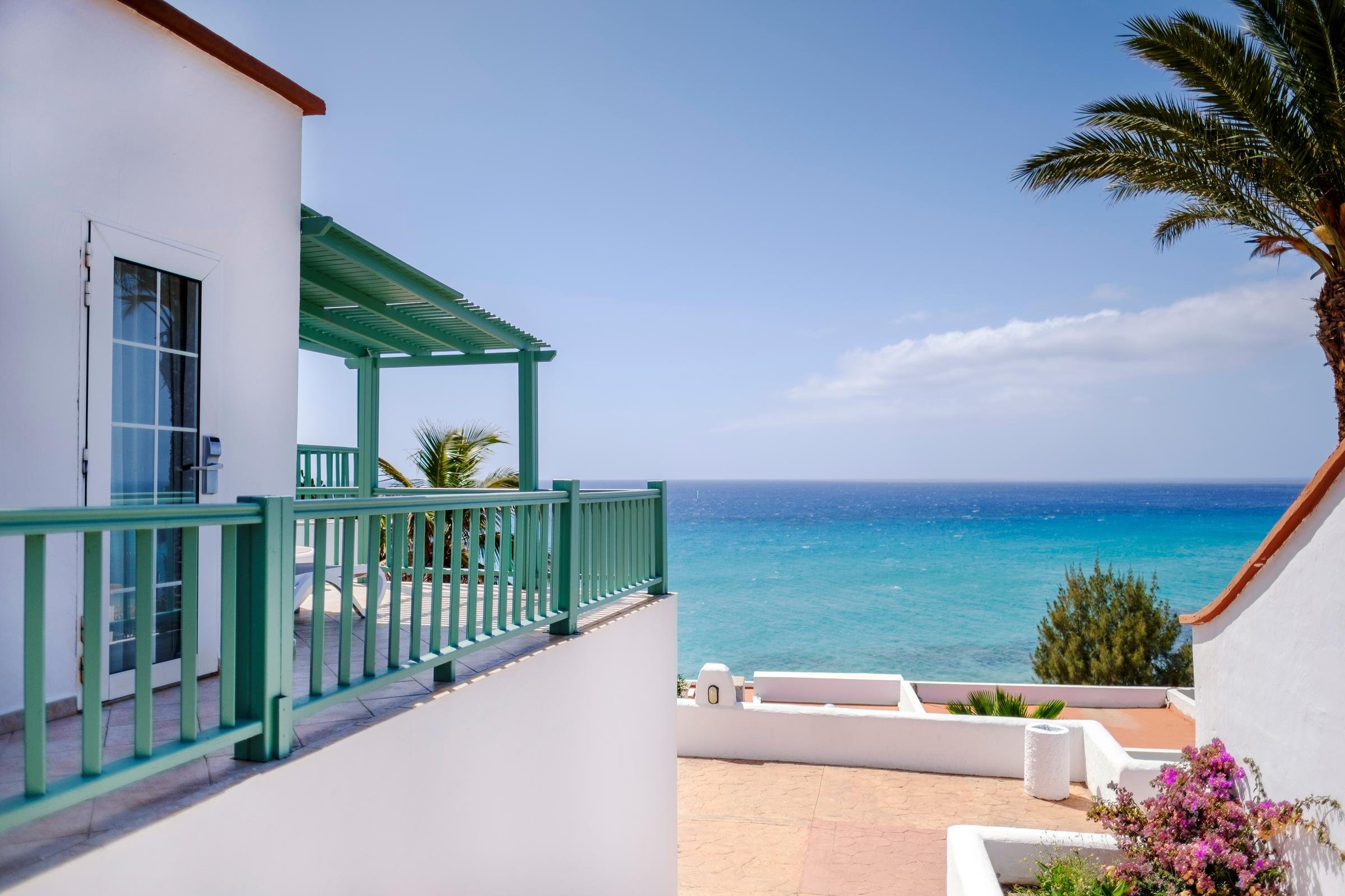 Ein sonniger Blick auf das Meer, Palmen und eine elegante weiße Gebäudeanlage.