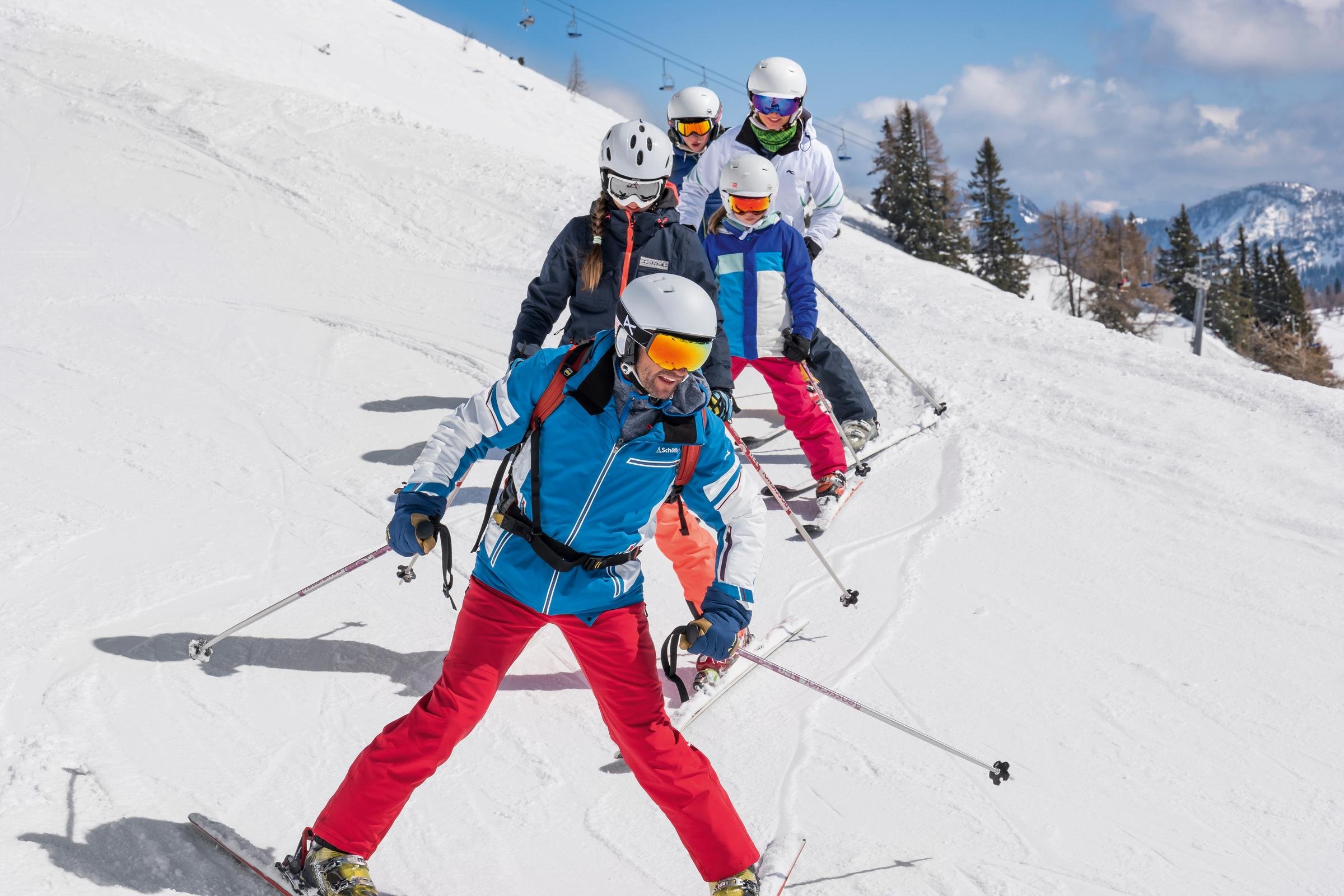 Vier Skifahrer in bunt gekleideter Gruppe auf verschneitem Hang mit Berglandschaft im Hintergrund