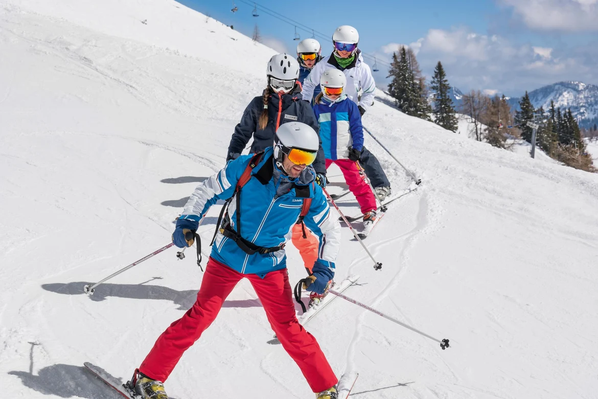 Vier Skifahrer in bunt gekleideter Gruppe auf verschneitem Hang mit Berglandschaft im Hintergrund