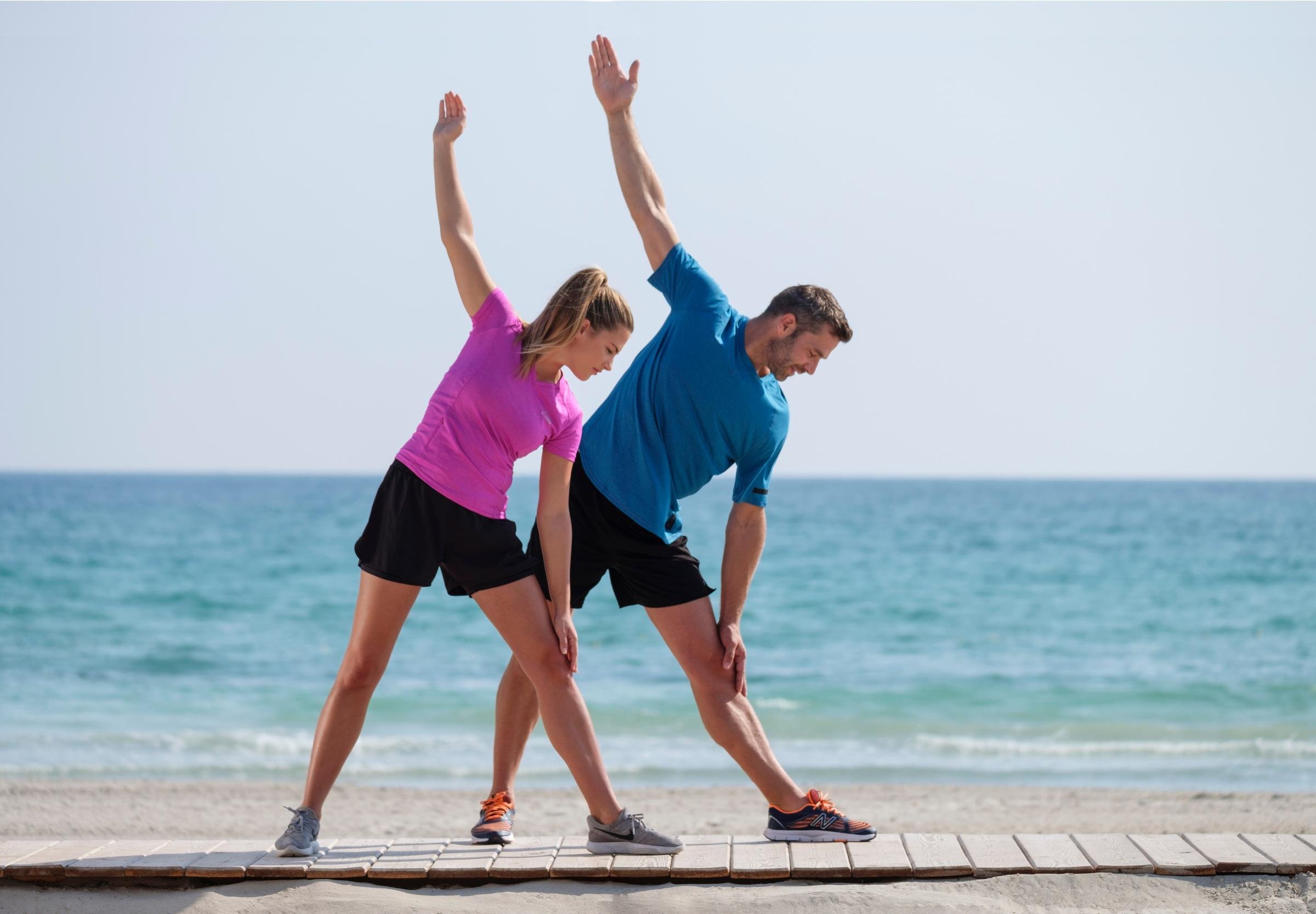 Zwei Menschen dehnen sich am Strand im Premium Cluburlaub von Aldiana.