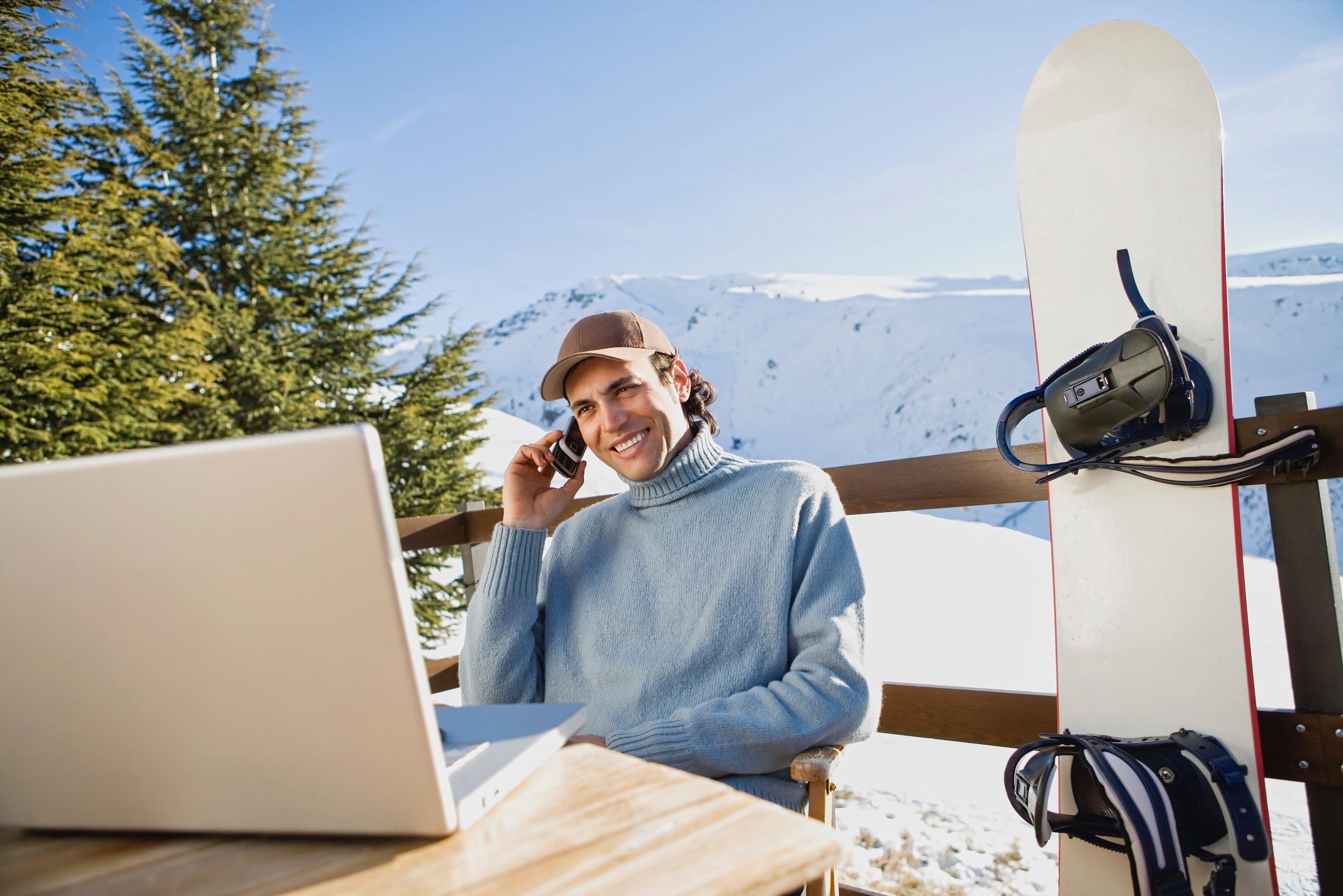 Frau mit Winterbekleidung und Snowboard beim Arbeiten mit Laptop im Schneewinterurlaub