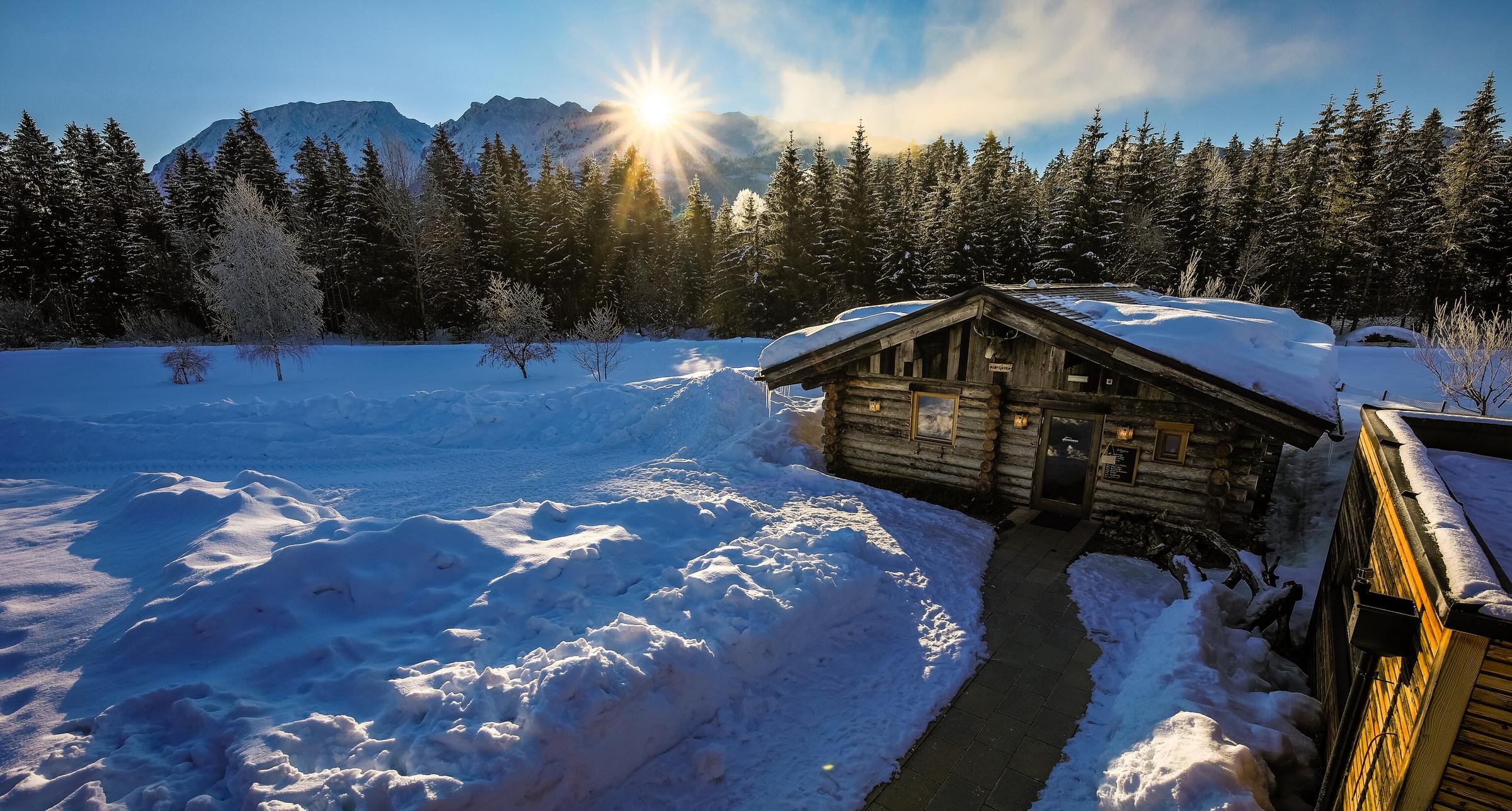 Eine verschneite Winterlandschaft mit Holzhaus, Bergen und Sonnenaufgang, ideal für Premium Cluburlaub