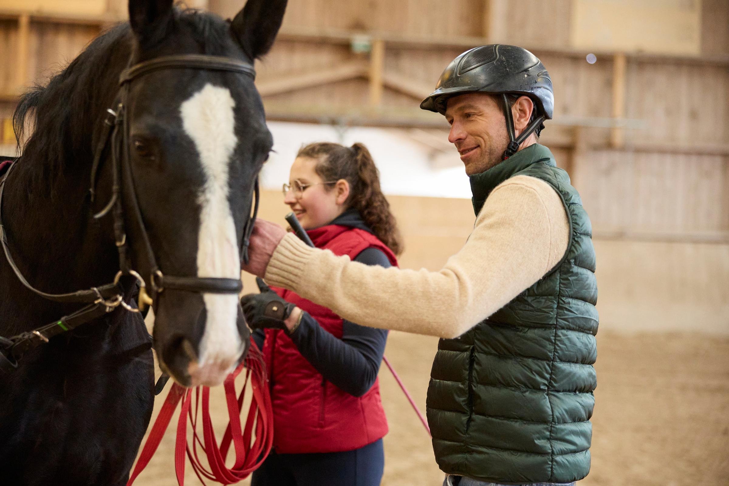 Zwei Personen streicheln ein schwarzes Pferd in einer Reithalle bei Aldiana.