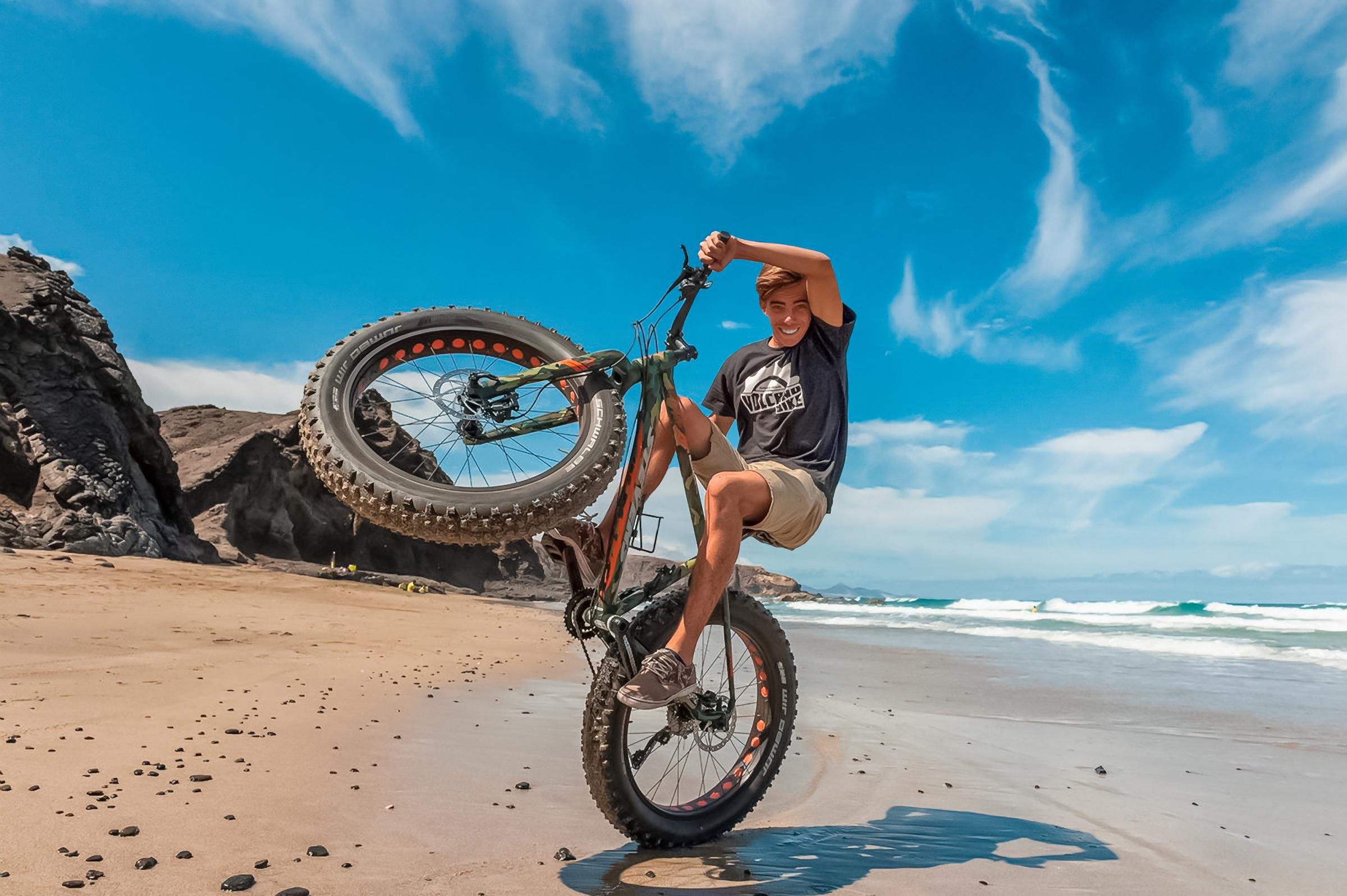 Ein junger Mann macht eine Fahrrad-Obstakel am Strand bei Sonnenlicht