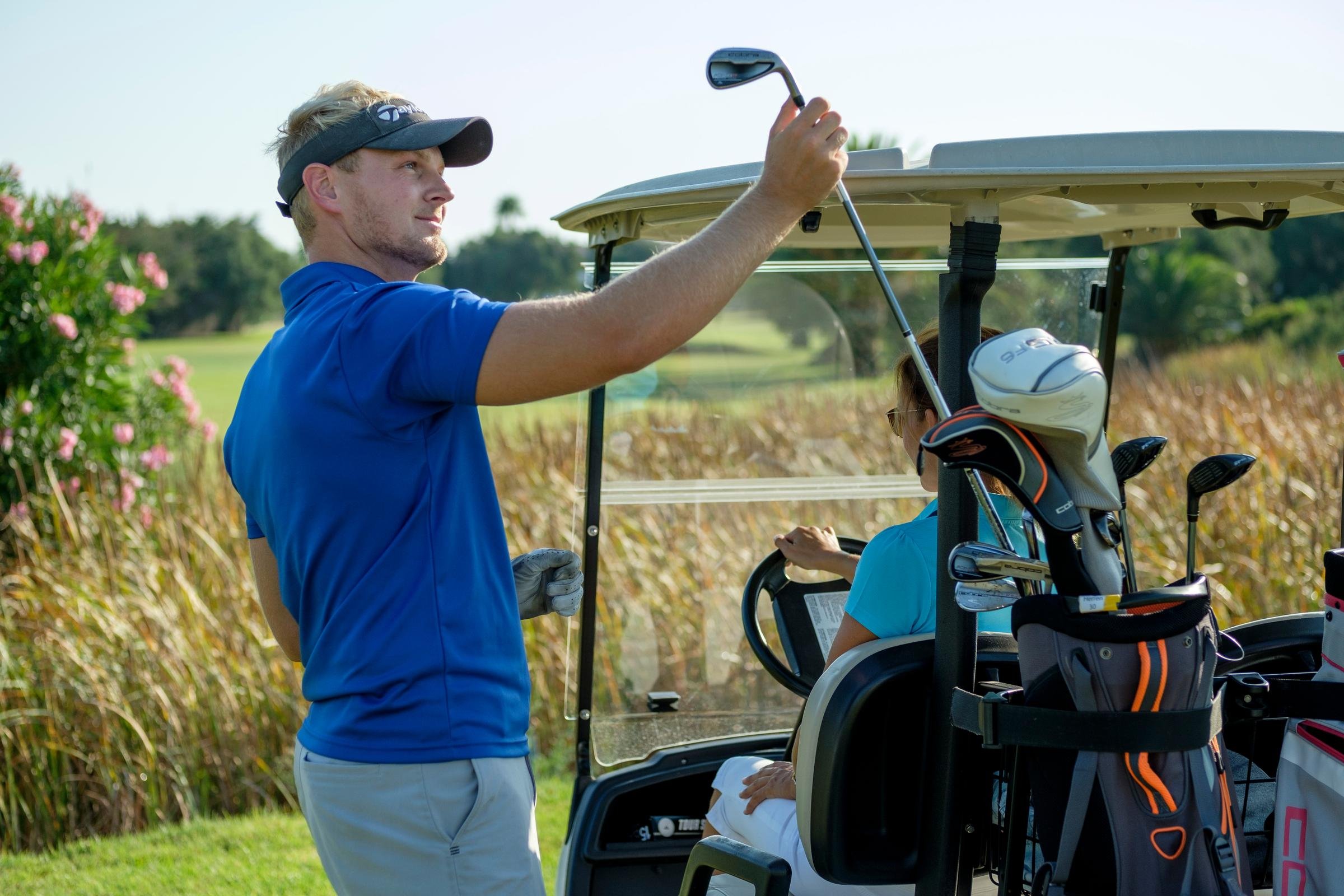 Golfspieler auf dem Golfplatz mit Golfschlägern und Golfwagen in einer urlaubsähnlichen Umgebung
