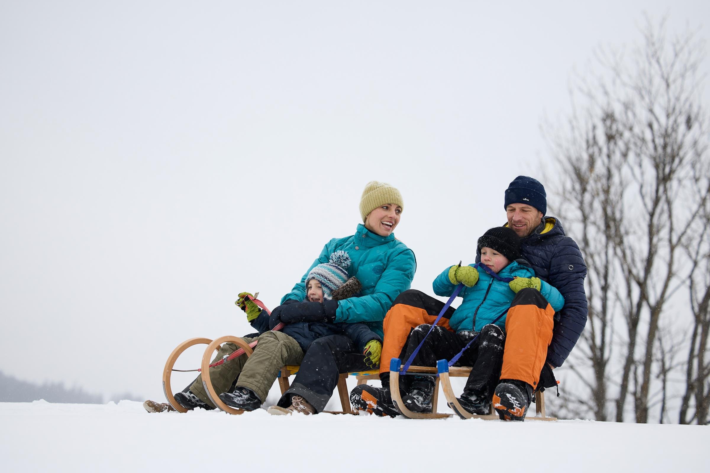 Familien beim Winterurlaub auf schneebedeitem Gelände mit Schlitten, Winterkleidung und Bäumen
