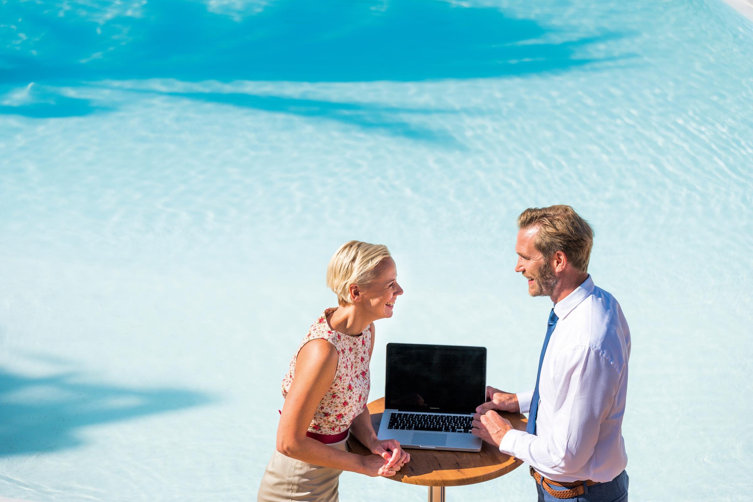 Ein Mann und eine Frau sprechen am Strand mit Laptop, Urlaubsatmosphäre, Premium Cluburlaub