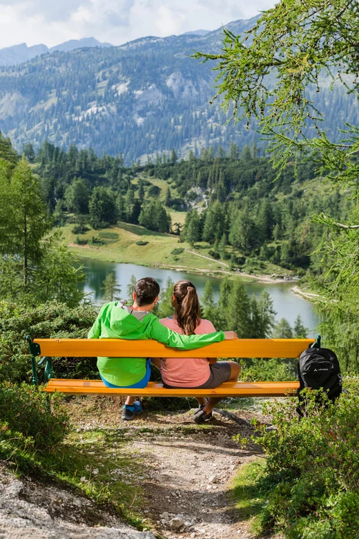 Zwei Personen sitzen auf einer Bank am See mit Bergblick, Ruhe und Natur genießen