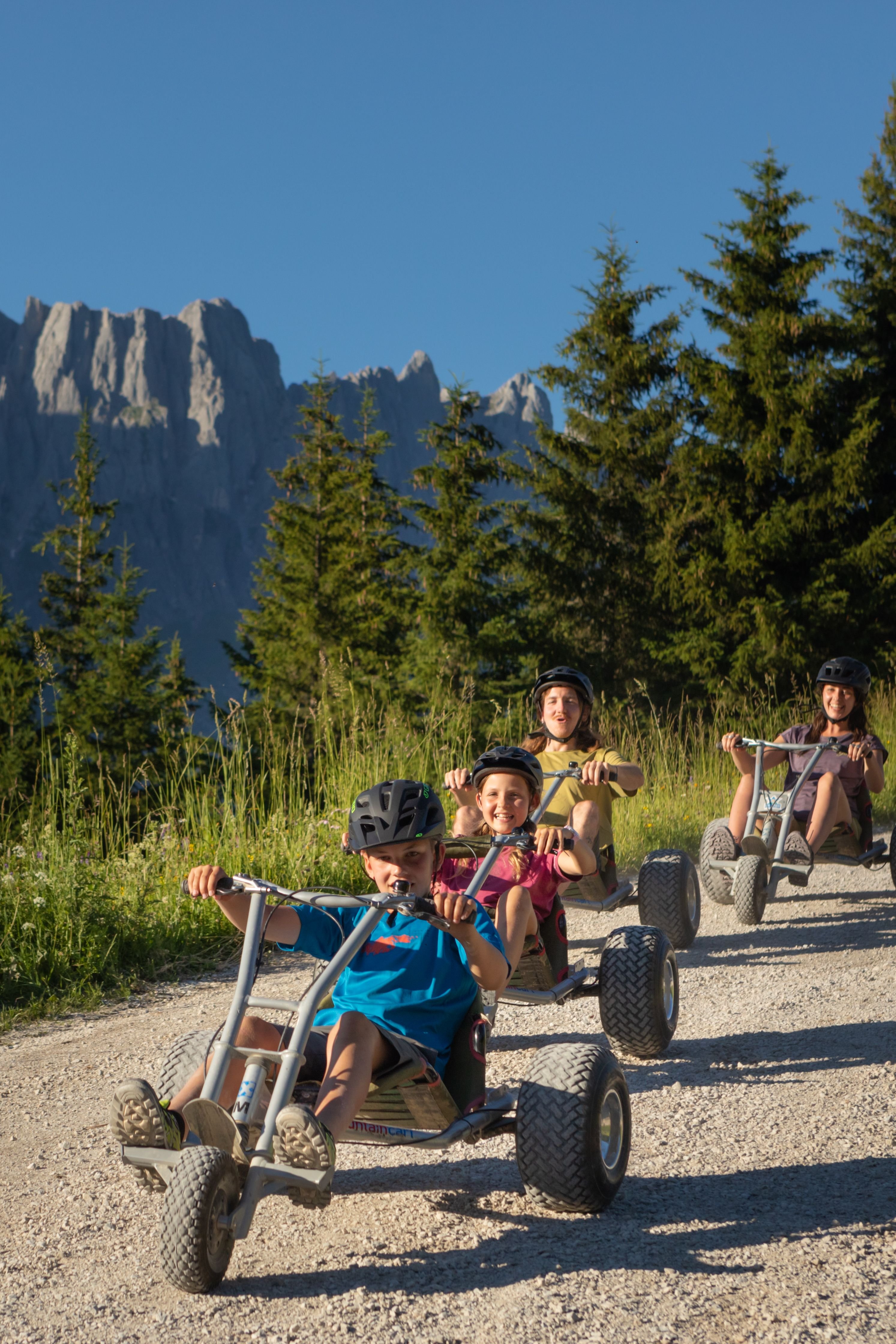 Kinder fahren auf go-karts mit Panoramablick auf Berge und Wälder bei Sonnenlicht
