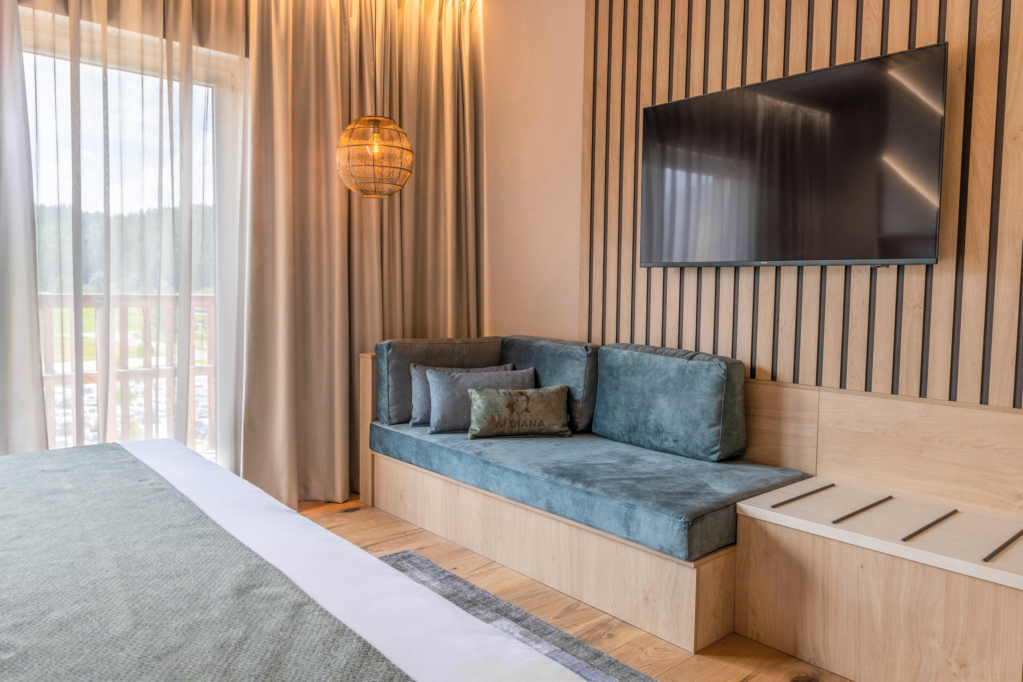 Gemütliches Hotelzimmer mit Sofa, Fernseher und Blick auf den Balkon