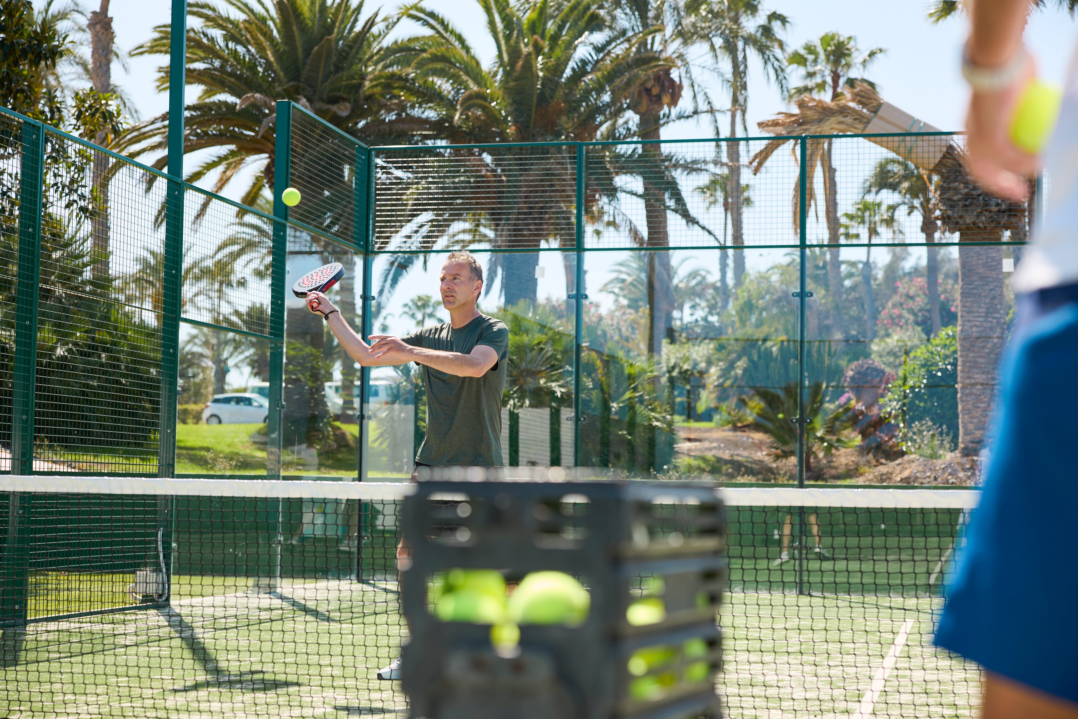 Turnierende Person beim Tennisspielen auf einem Tennisplatz im sonnigen Park mit Palmen