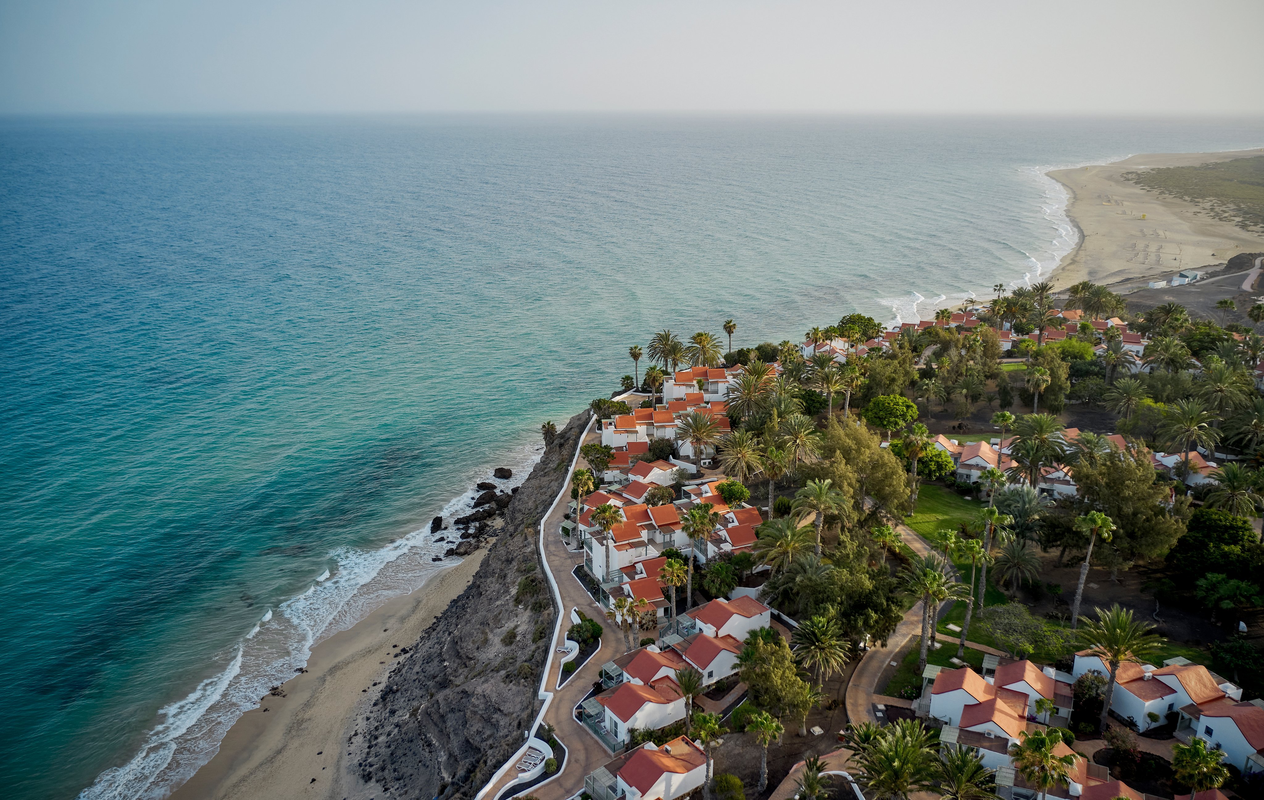 Blick auf eine exklusive Urlaubsanlage am Strand mit Pool und Palmen, Luxus und Entspannung