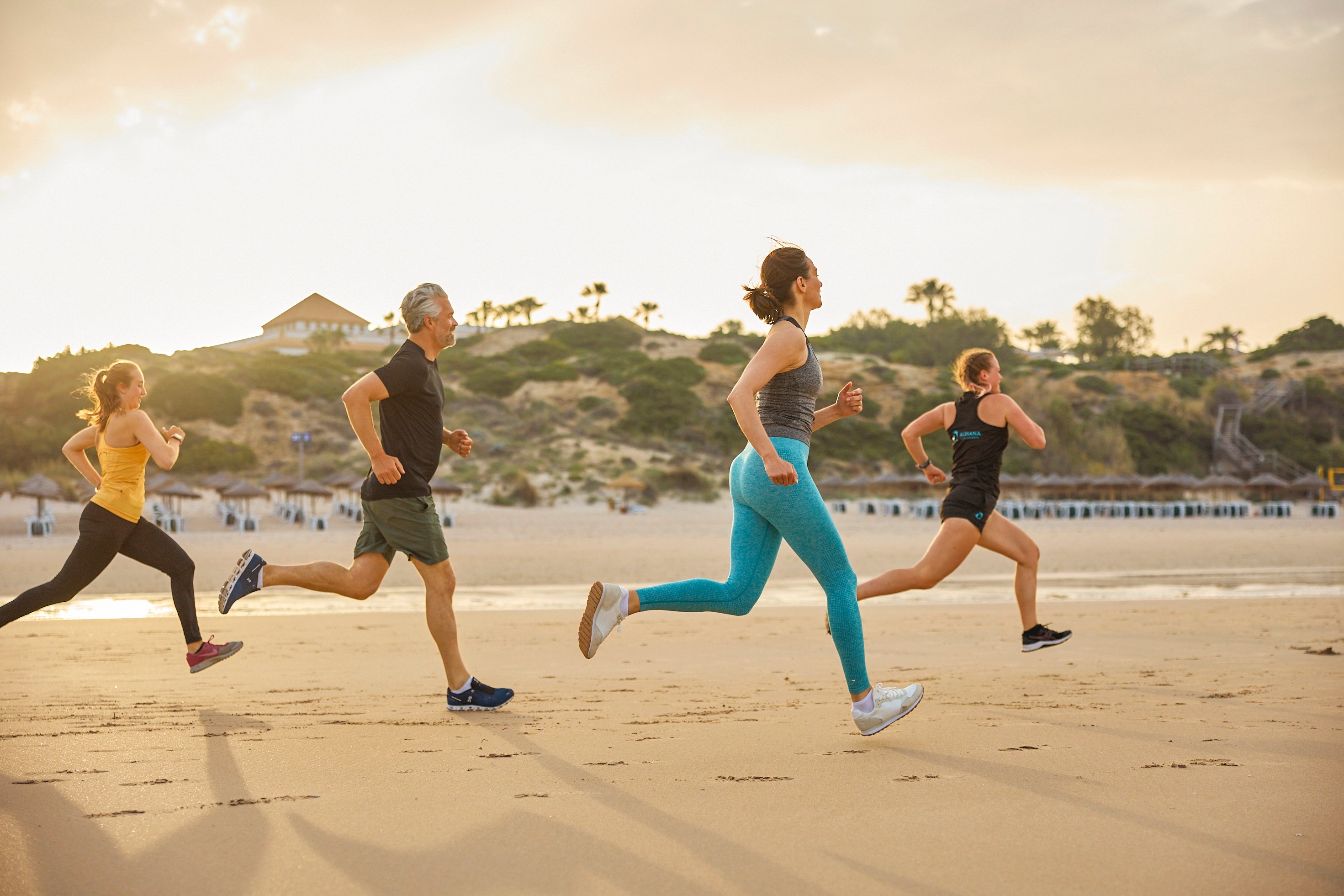 Menschen laufen am Strand bei Sonnenuntergang, genießen einen aktiven Premium Cluburlaub.