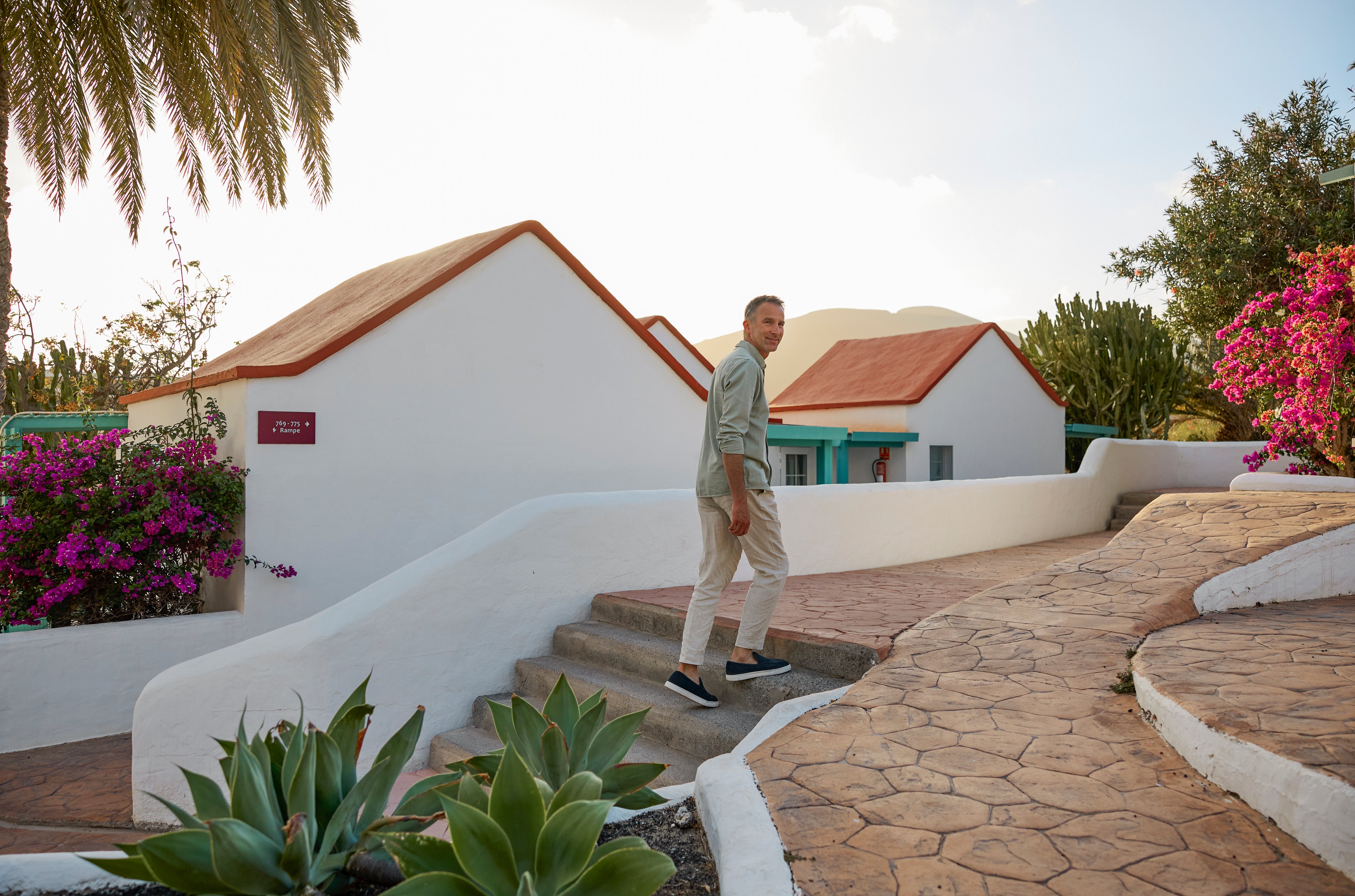 Mann beim Premium Cluburlaub von Aldiana auf gepflegtem Weg mit weißen Gebäuden und Pflanzen