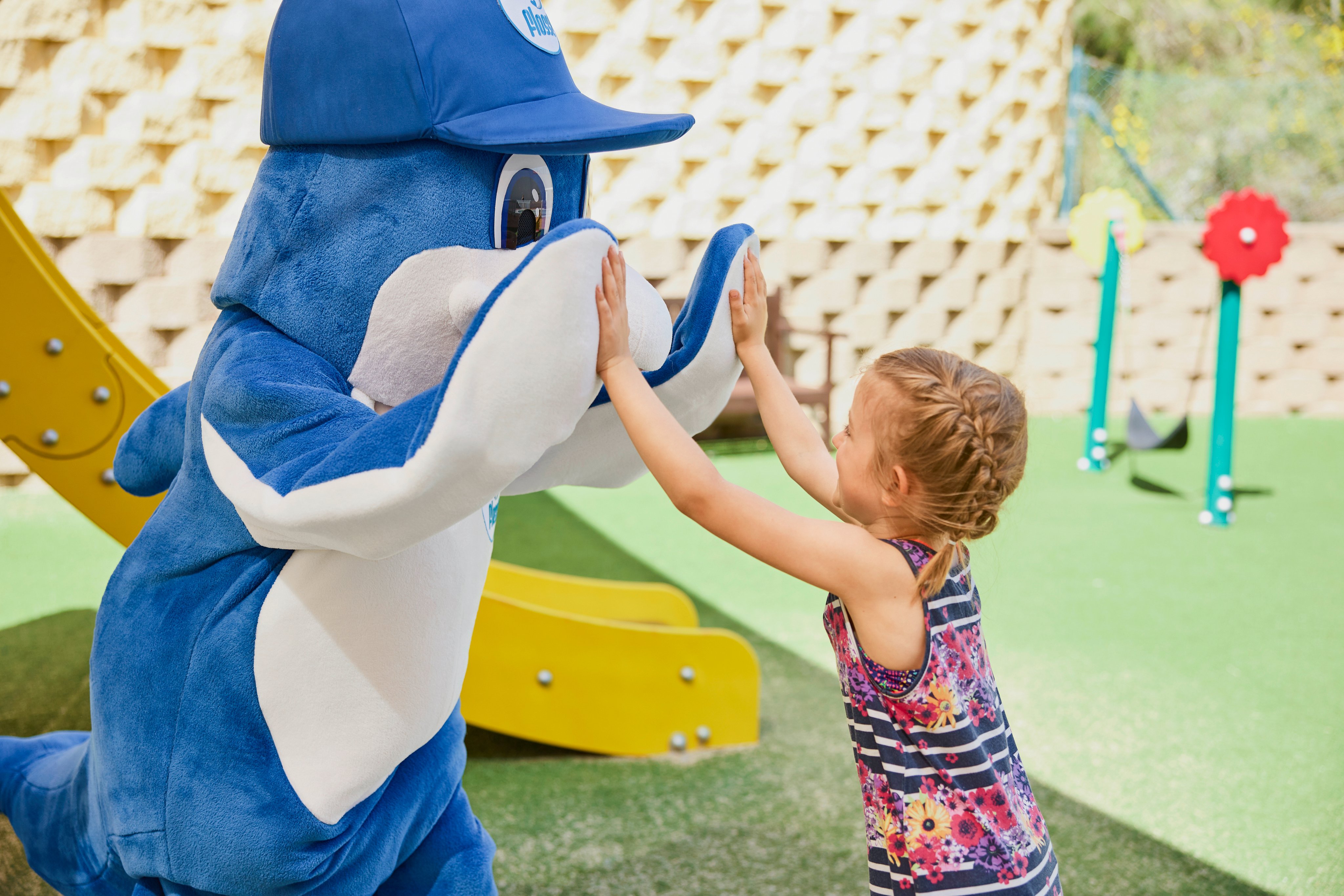 Kindergartenkind highfivend mit maskottchen im Außenbereich des Premium Cluburlaubs von Aldiana