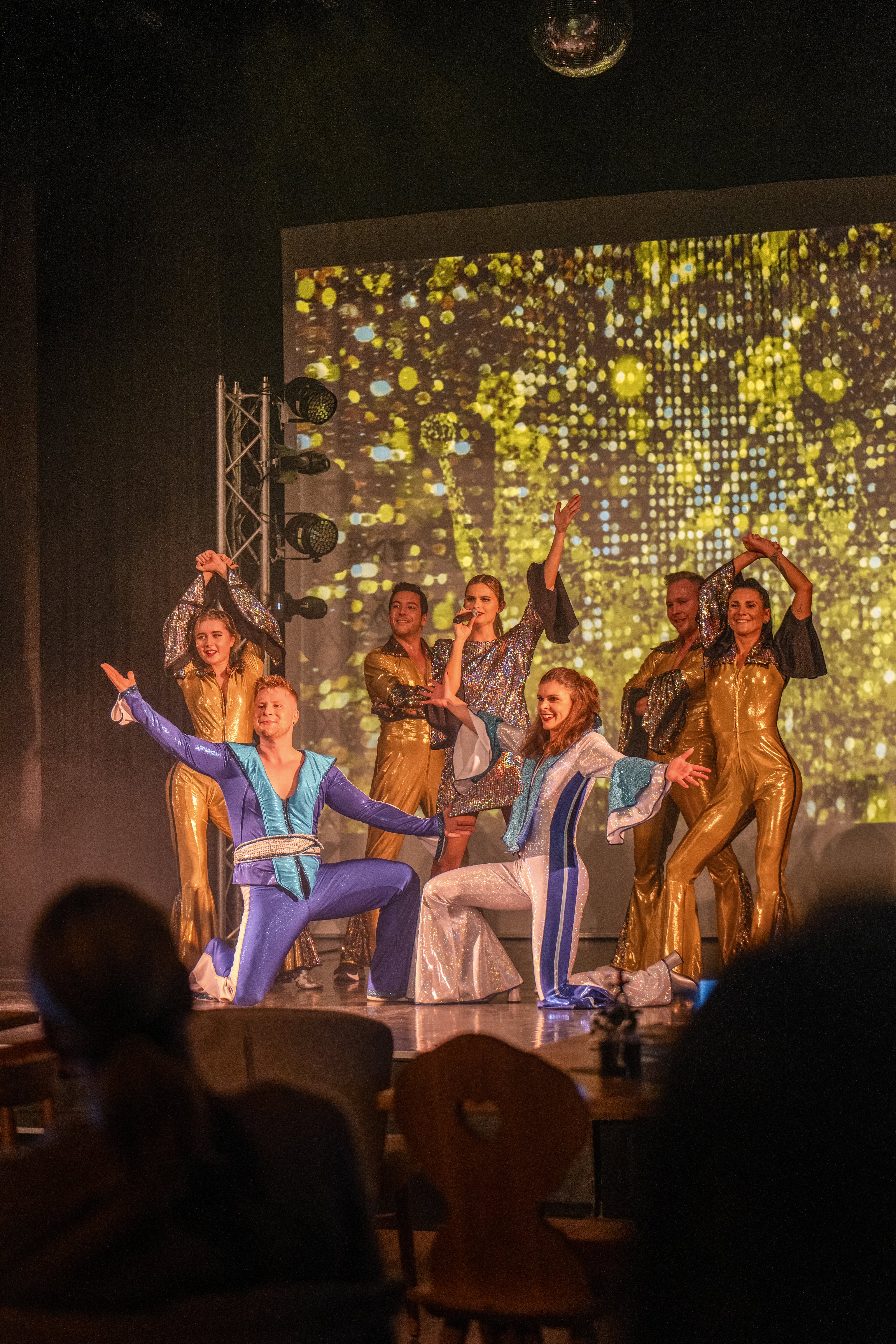 Tänzer auf Bühne bei Aldiana Show, goldene Kostüme, bunter Hintergrund, lebendige Atmosphäre