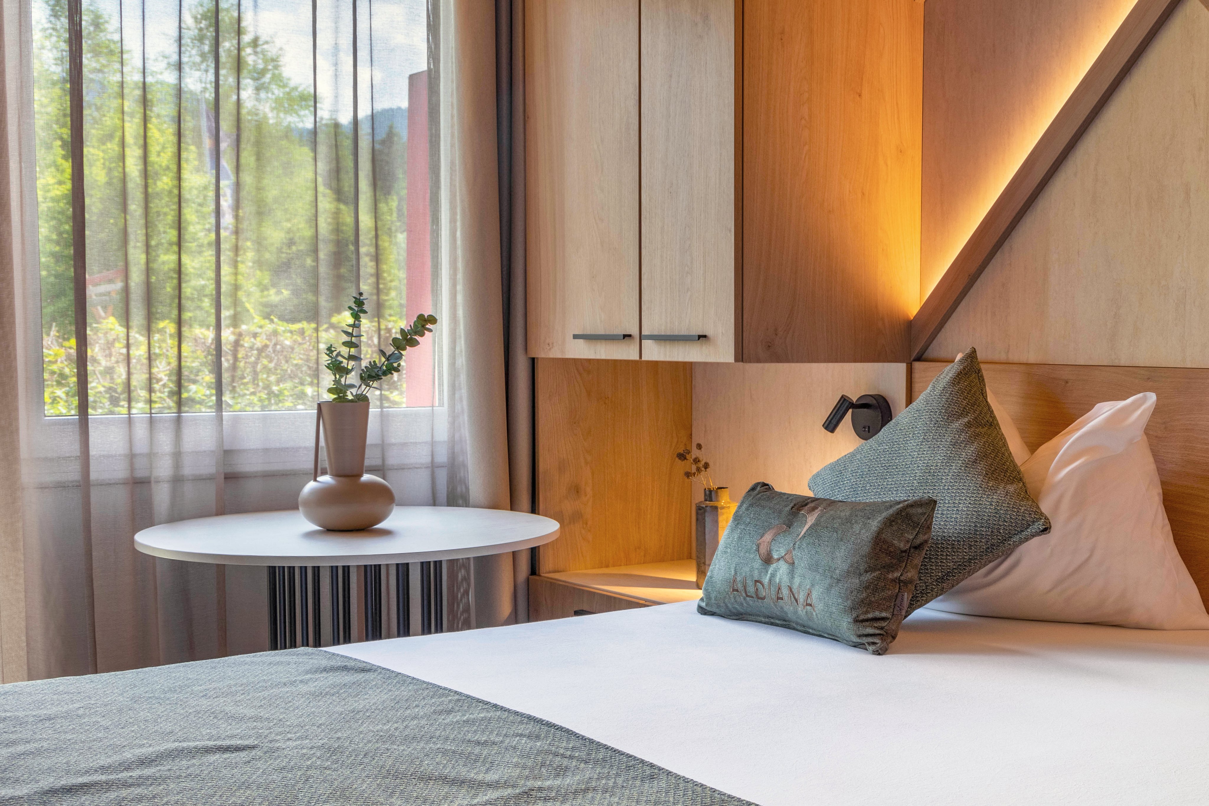 Ein modernes Hotelzimmer mit Bett, Nachttisch, Pflanzen und Fenster mit Vorhängen