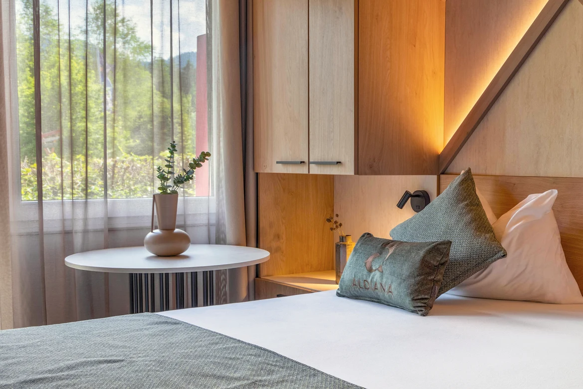 Ein modernes Hotelzimmer mit Bett, Nachttisch, Pflanzen und Fenster mit Vorhängen