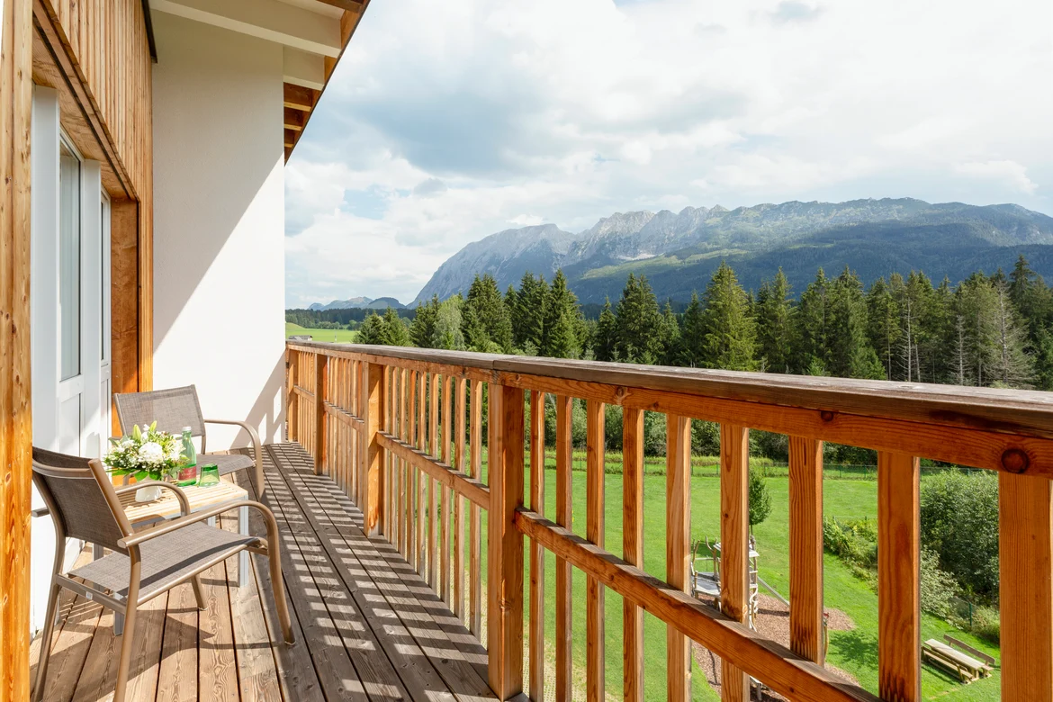 Balkon mit Holzgeländer und Terrassenmöbeln Blick auf Berge und grüne Landschaften
