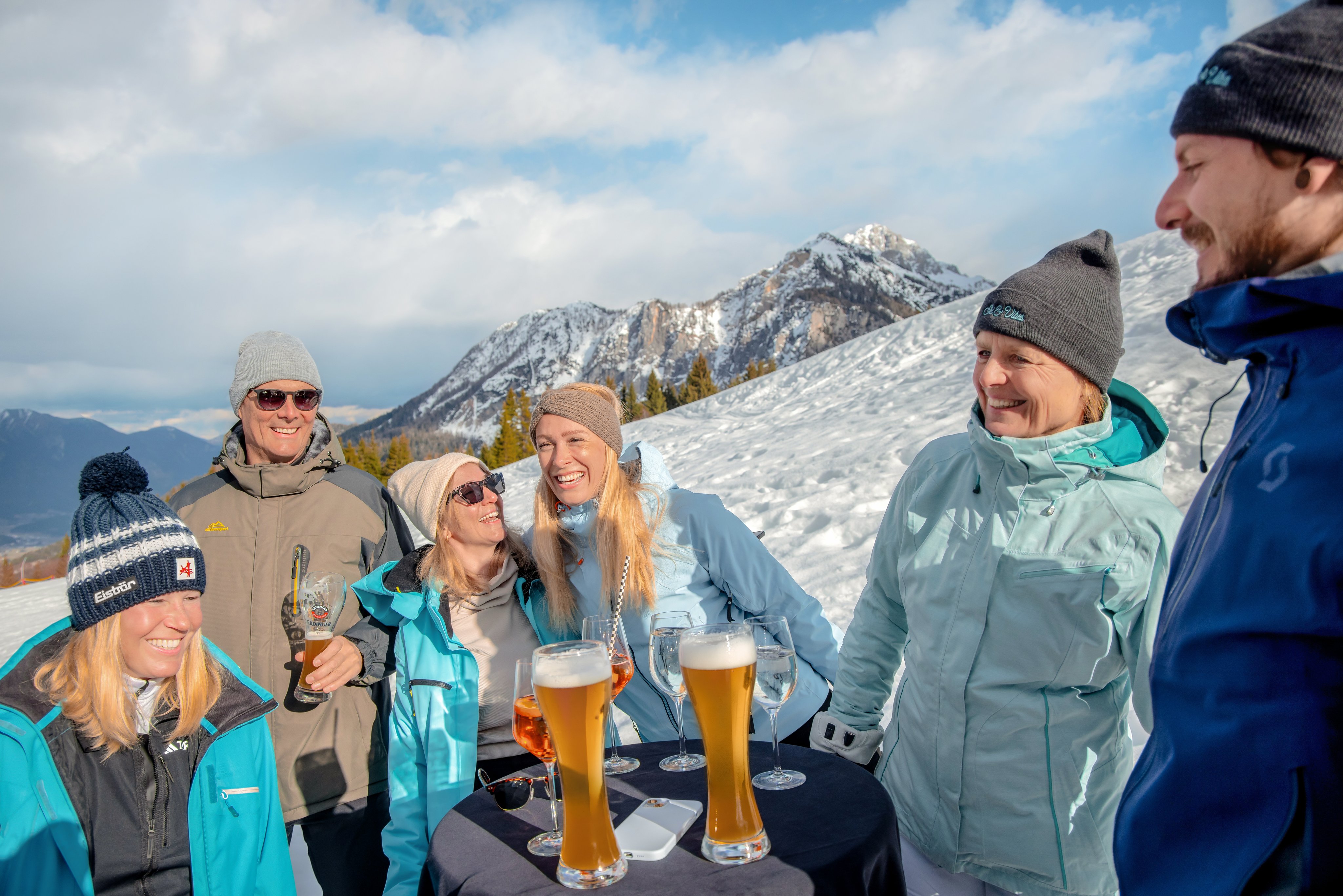 Gruppe von Menschen in Winterjacken und Mützen auf einer schneebedeckten Bergwiese mit Sehenswürdigkeit im Hintergrund