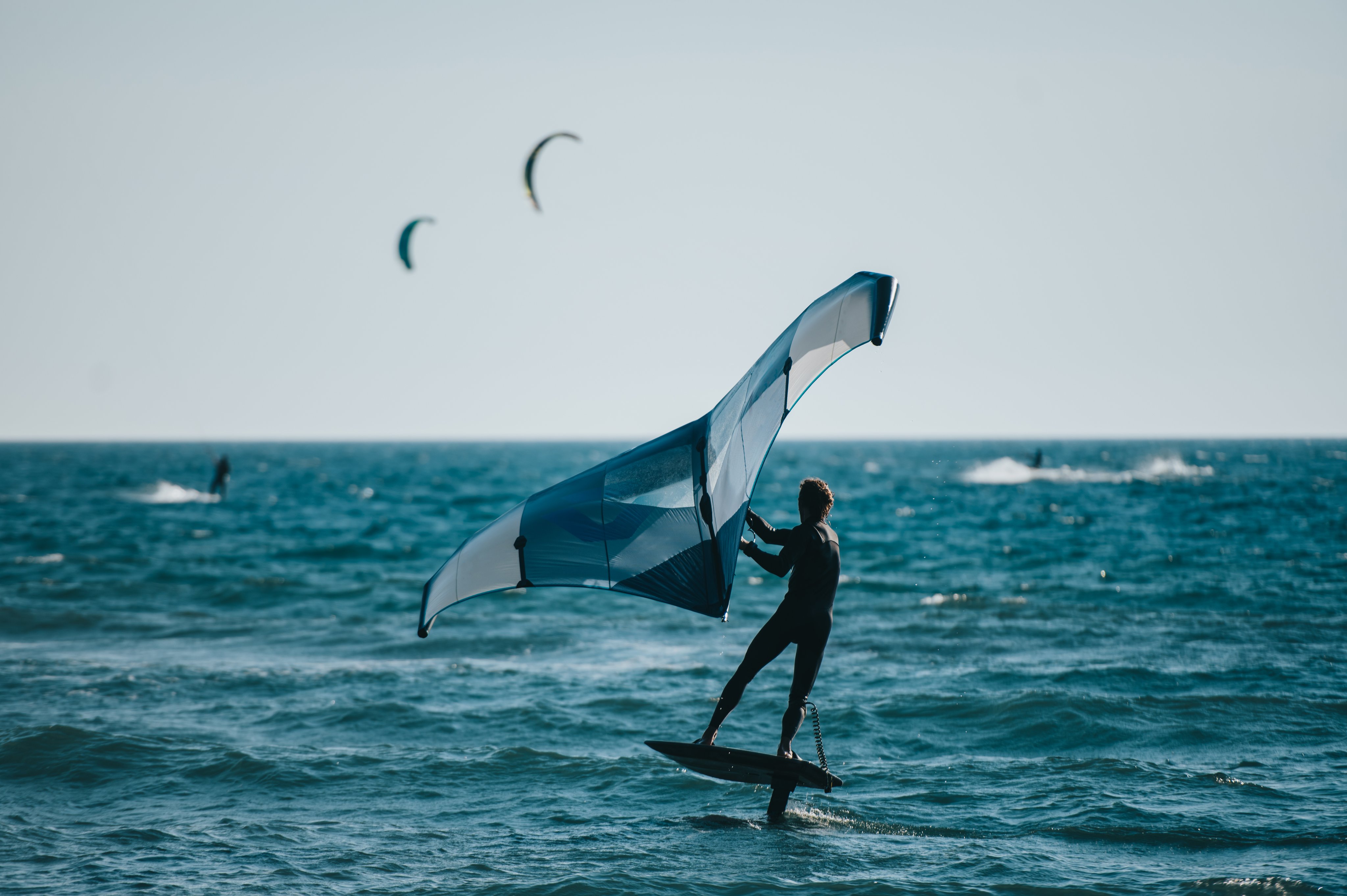 Ein Mensch beim Kitesurfen, Windfoiling auf dem Meer, blaues Tuch, sonniger Tag, Lifestyle Bild