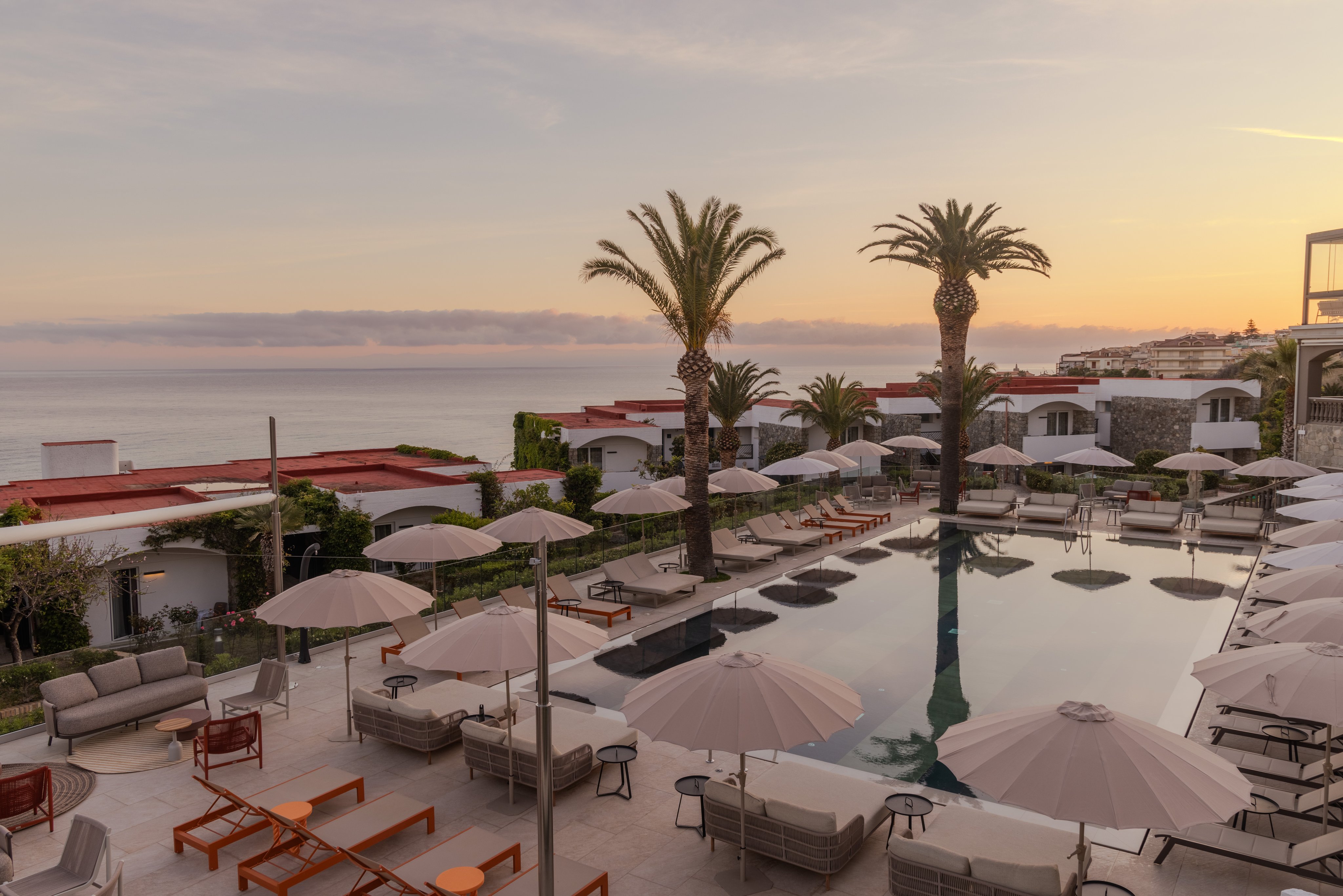 Schöner Poolbereich mit Liegen, Palmen und Blick auf das Meer bei Sonnenuntergang