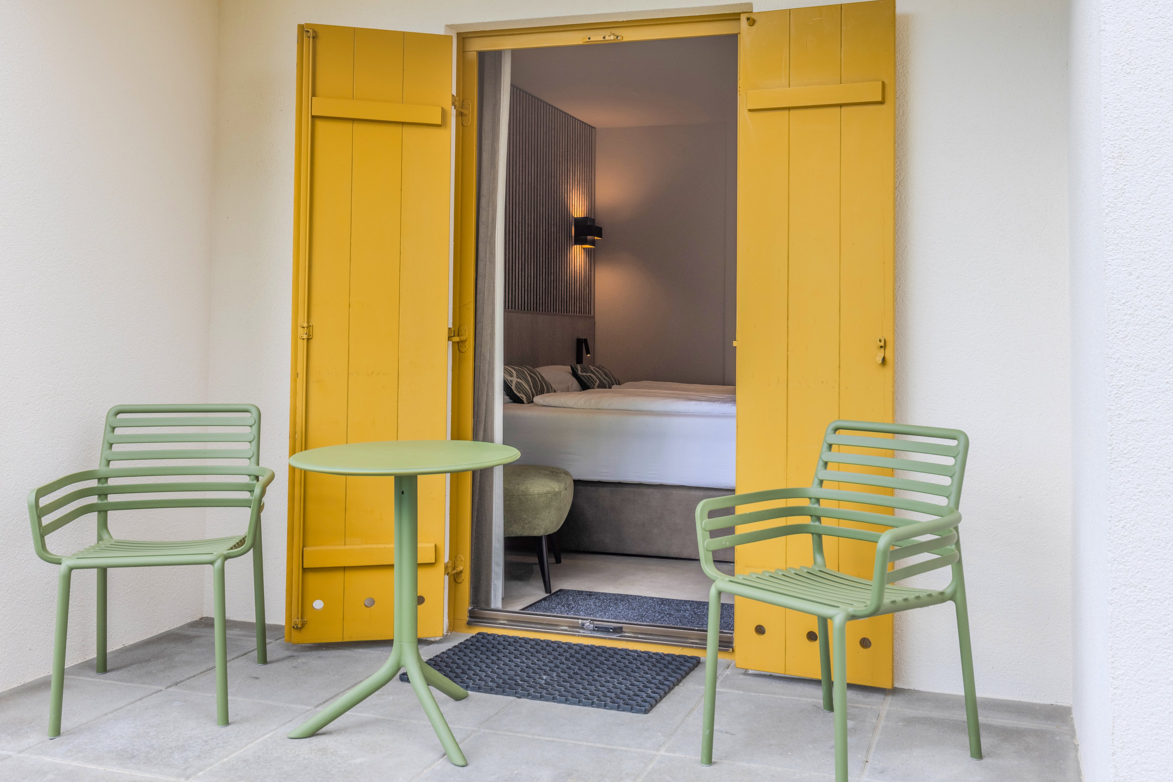 Blick in ein Hotelzimmer mit gelben Türen, Balkonmöbeln und einem bequemen Bett