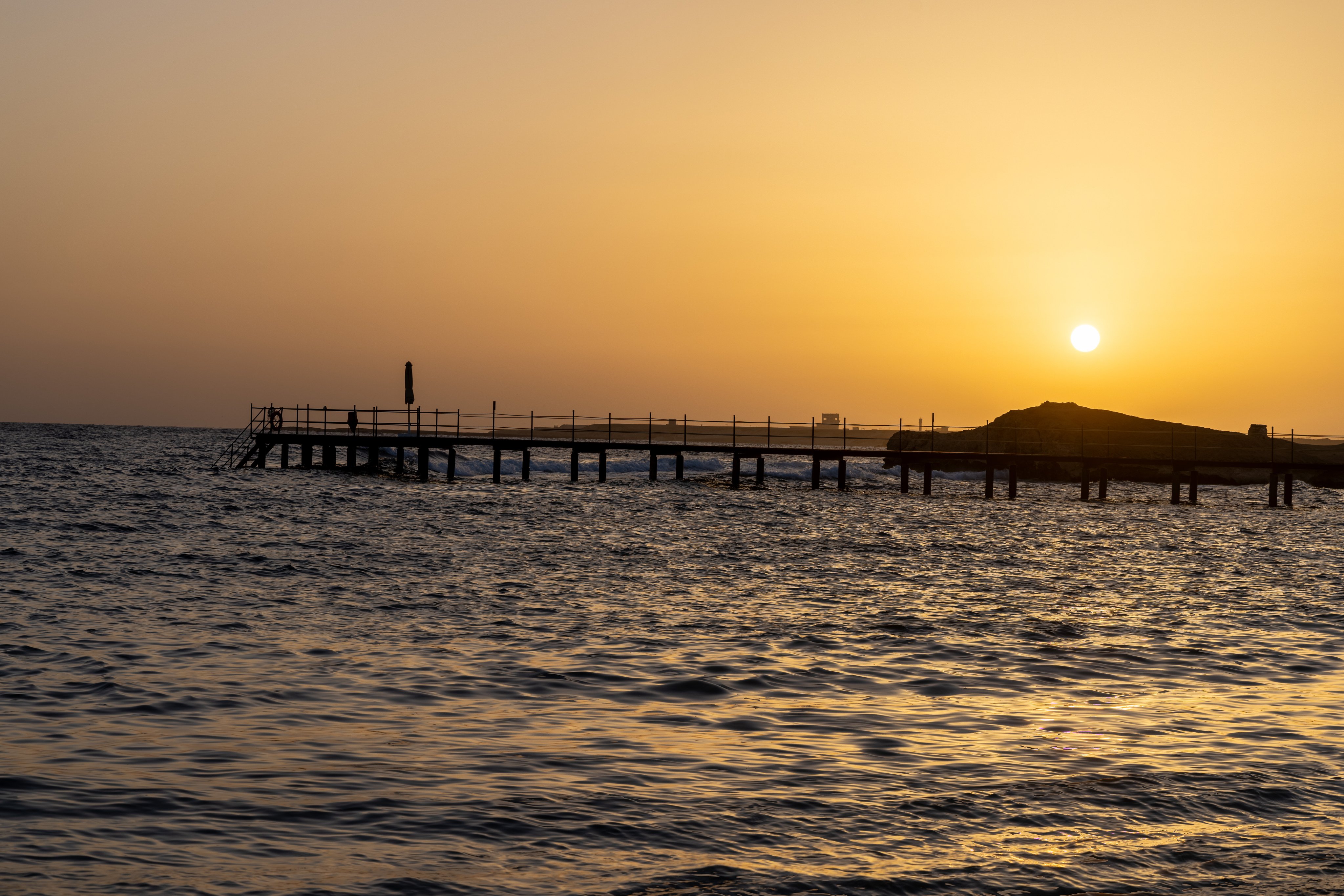 Ein ruhiger Sonnenuntergang am Strand mit Blick auf das Meer und einen Steg.