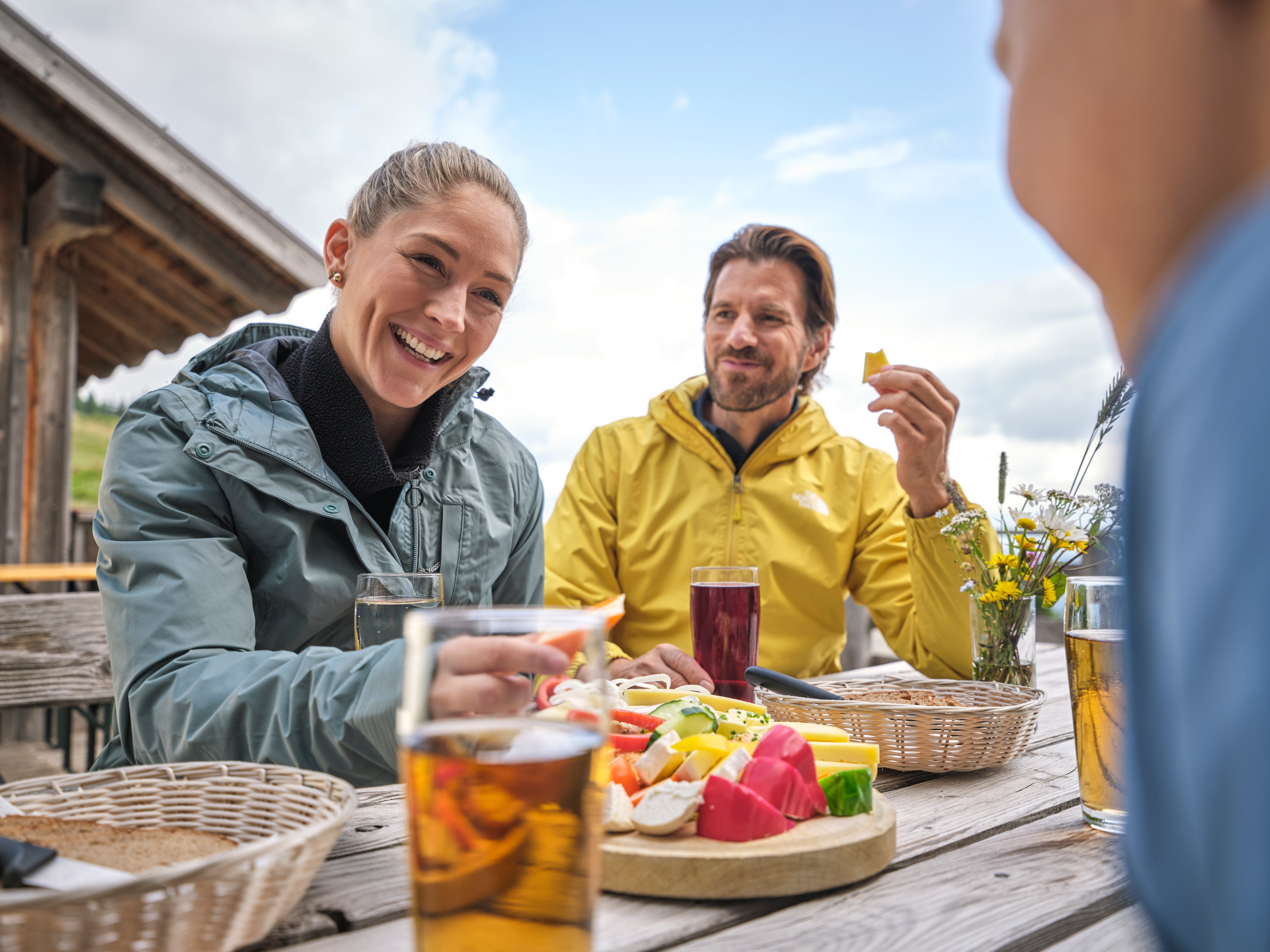 Drei Personen beim Picknick im Freien mit unterschiedlichen Getränken und Snacks