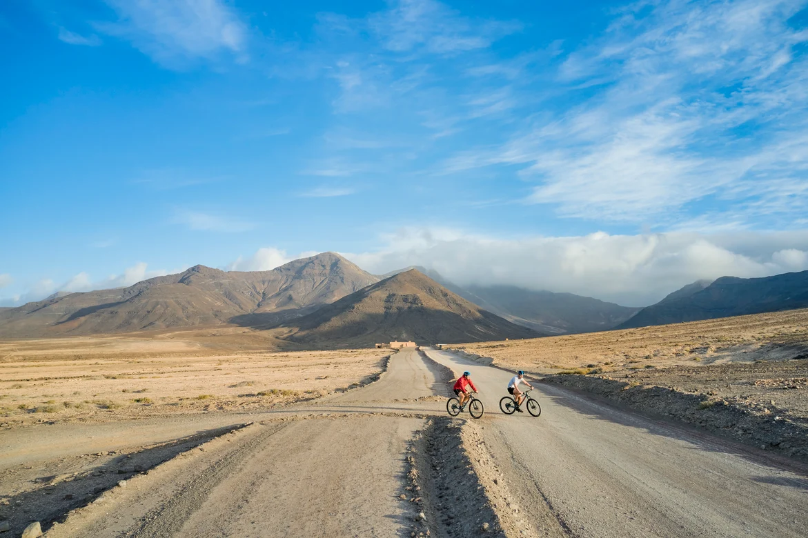 Zwei Kinder auf Fahrrädern in karger Landschaft mit Bergen im Hintergrund, ideales Familienabenteuer