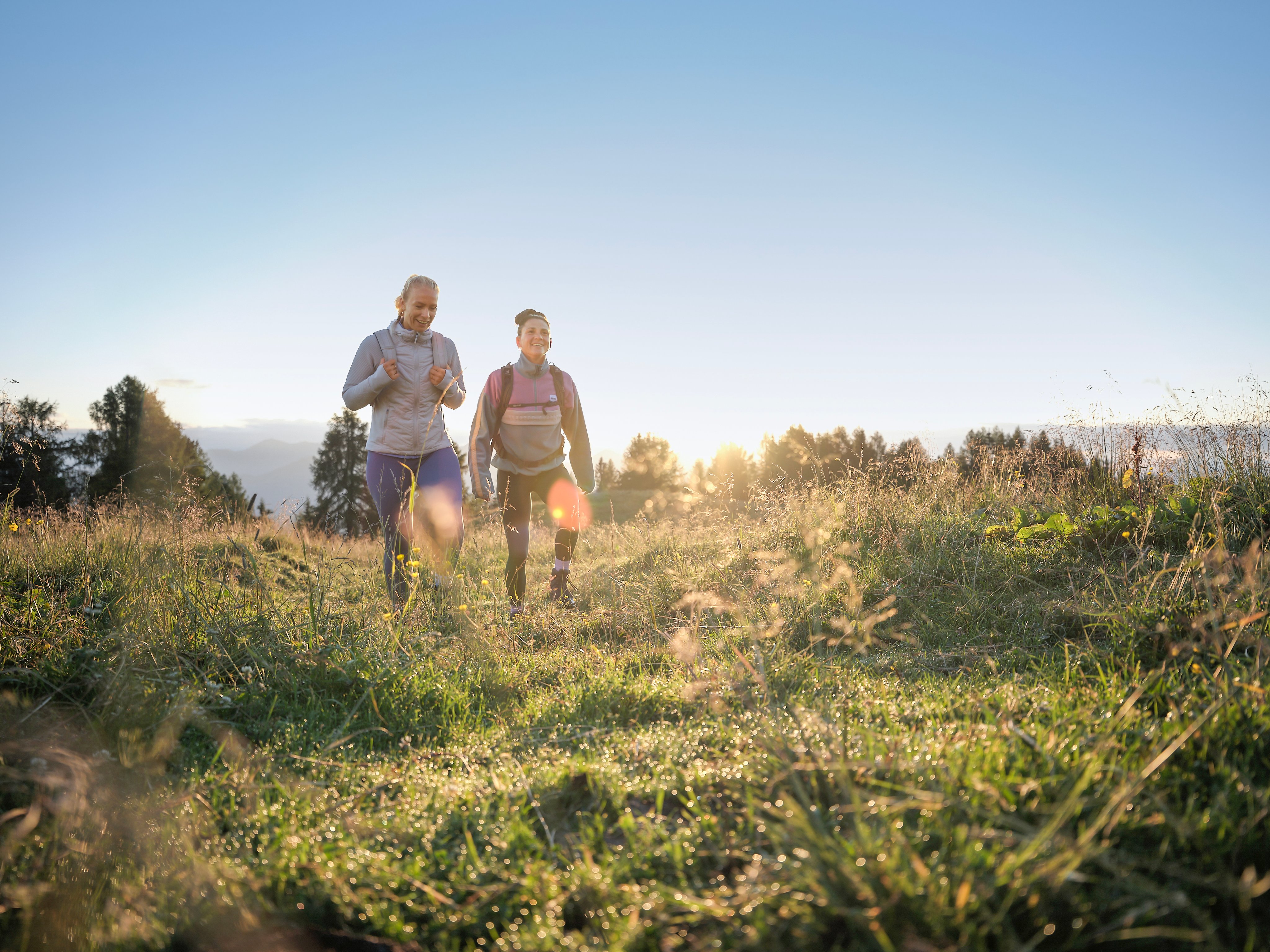 Zwei junge Frauen wandern in der Natur bei Sonnenuntergang, genießen Premium Cluburlaub bei Aldiana