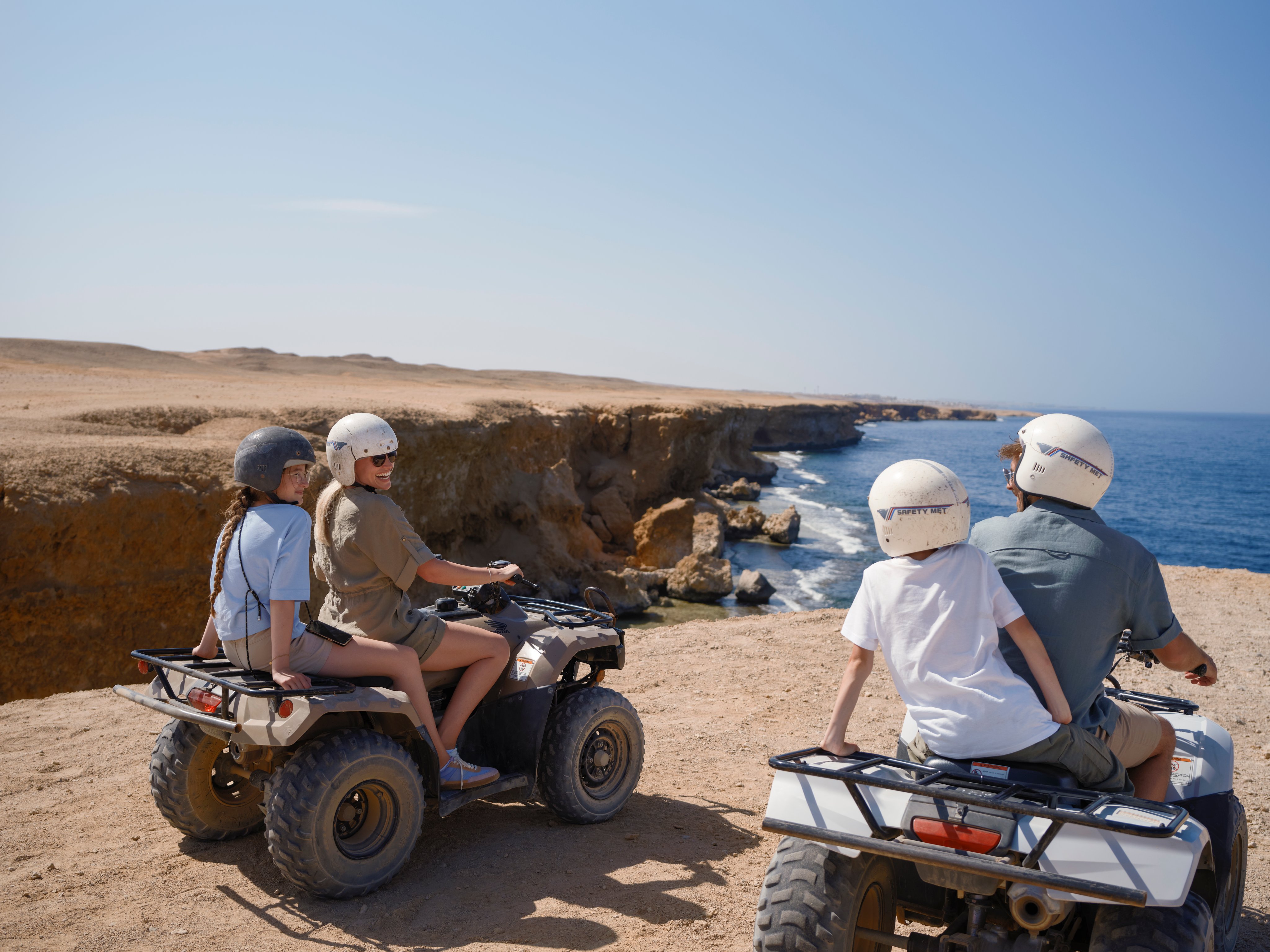 Zwei Erwachsene und zwei Kinder beim Quadfahren an der Küste, sonniger Tag, Urlaubsstimmung