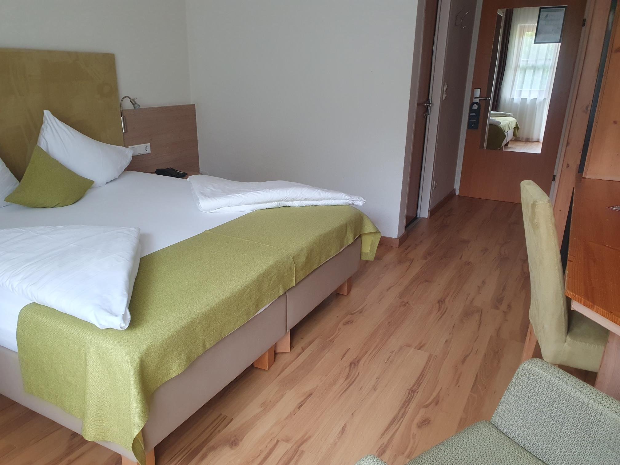 Schlafzimmer mit weißem Bett, grüner Bettdecke und Fenster in einer Hotelanlage