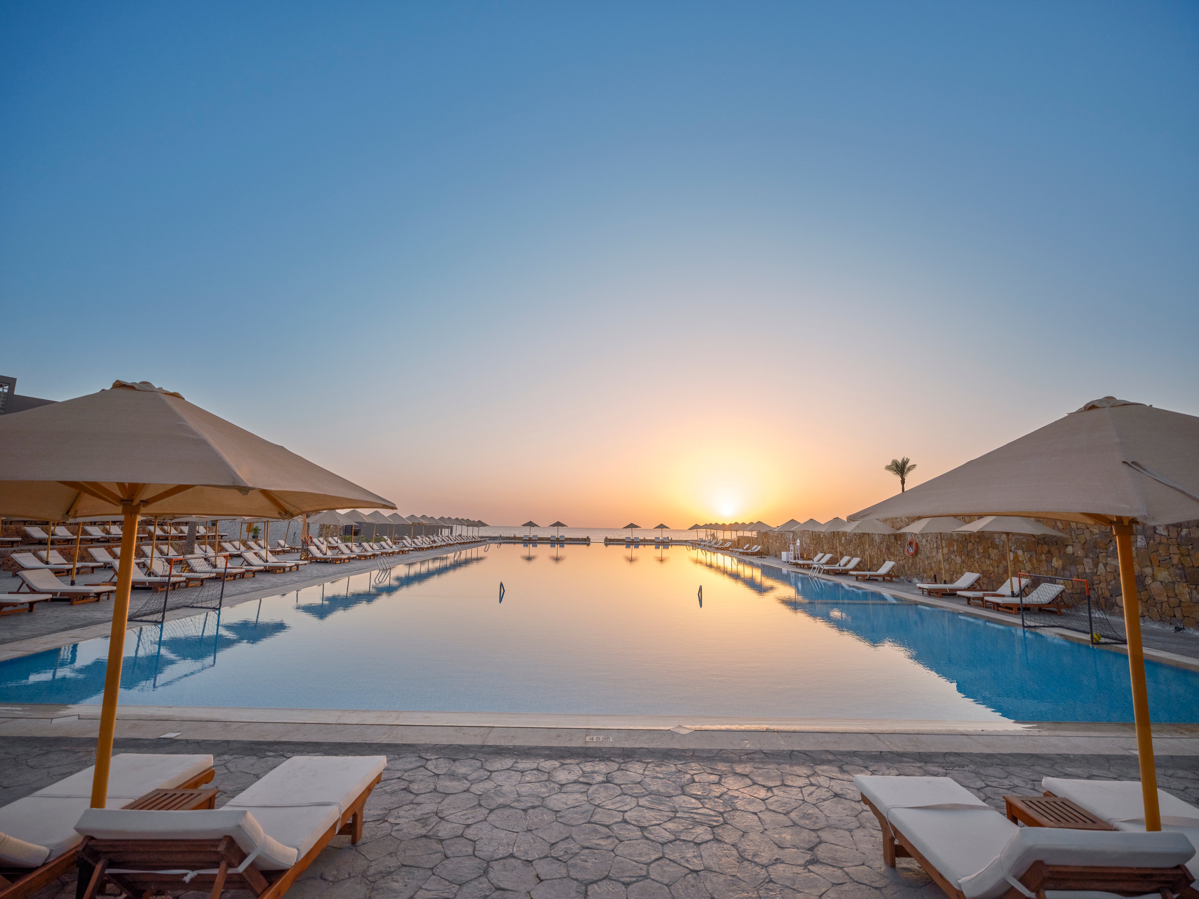 Entspannender Hotelpool mit Sonnenliegen und Sonnenschirmen bei Sonnenuntergang.