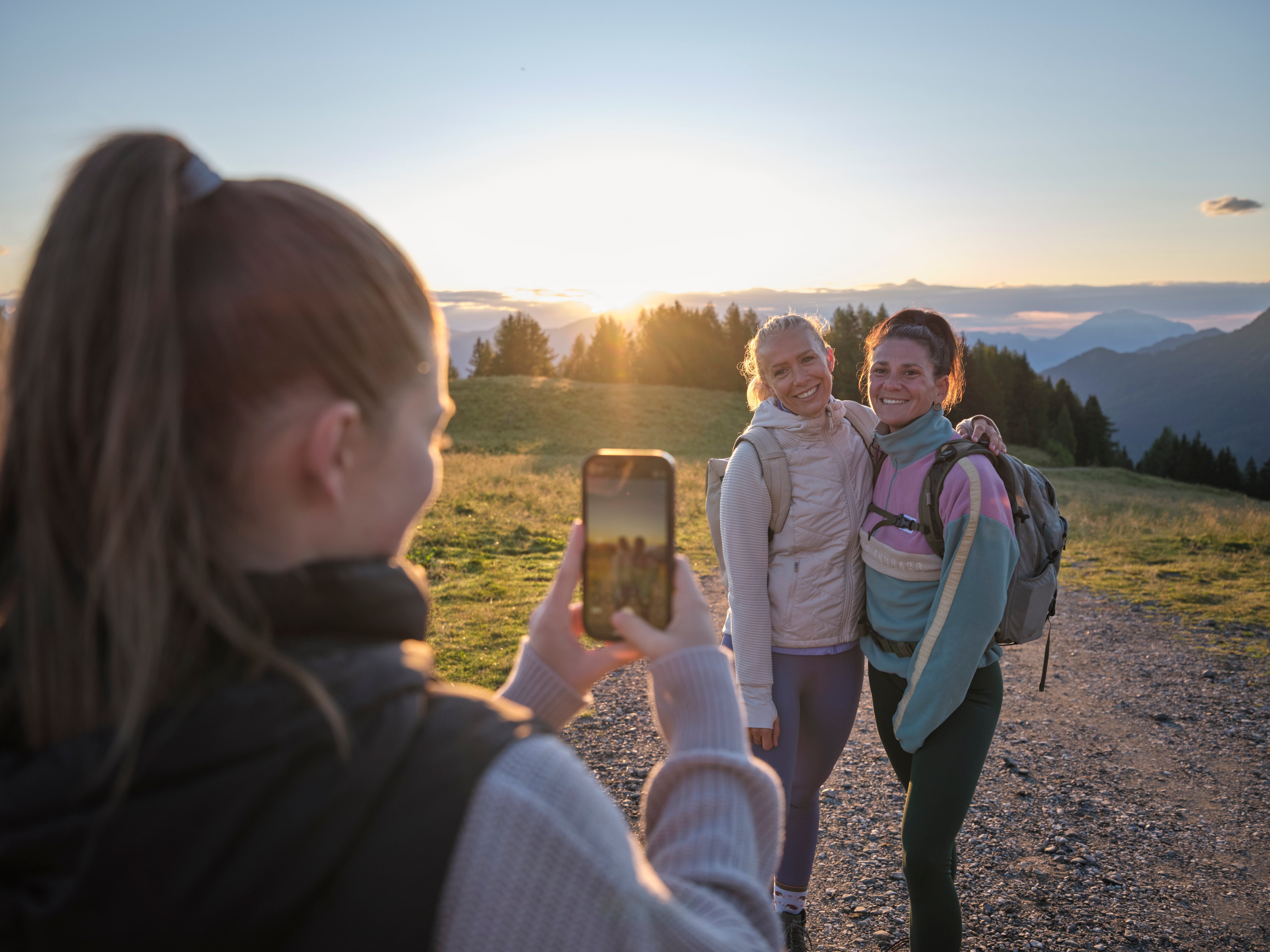 Zwei Frauen bei Sonnenuntergang im Naturpark, eine filmt das andere Paar, smart und entspannt.