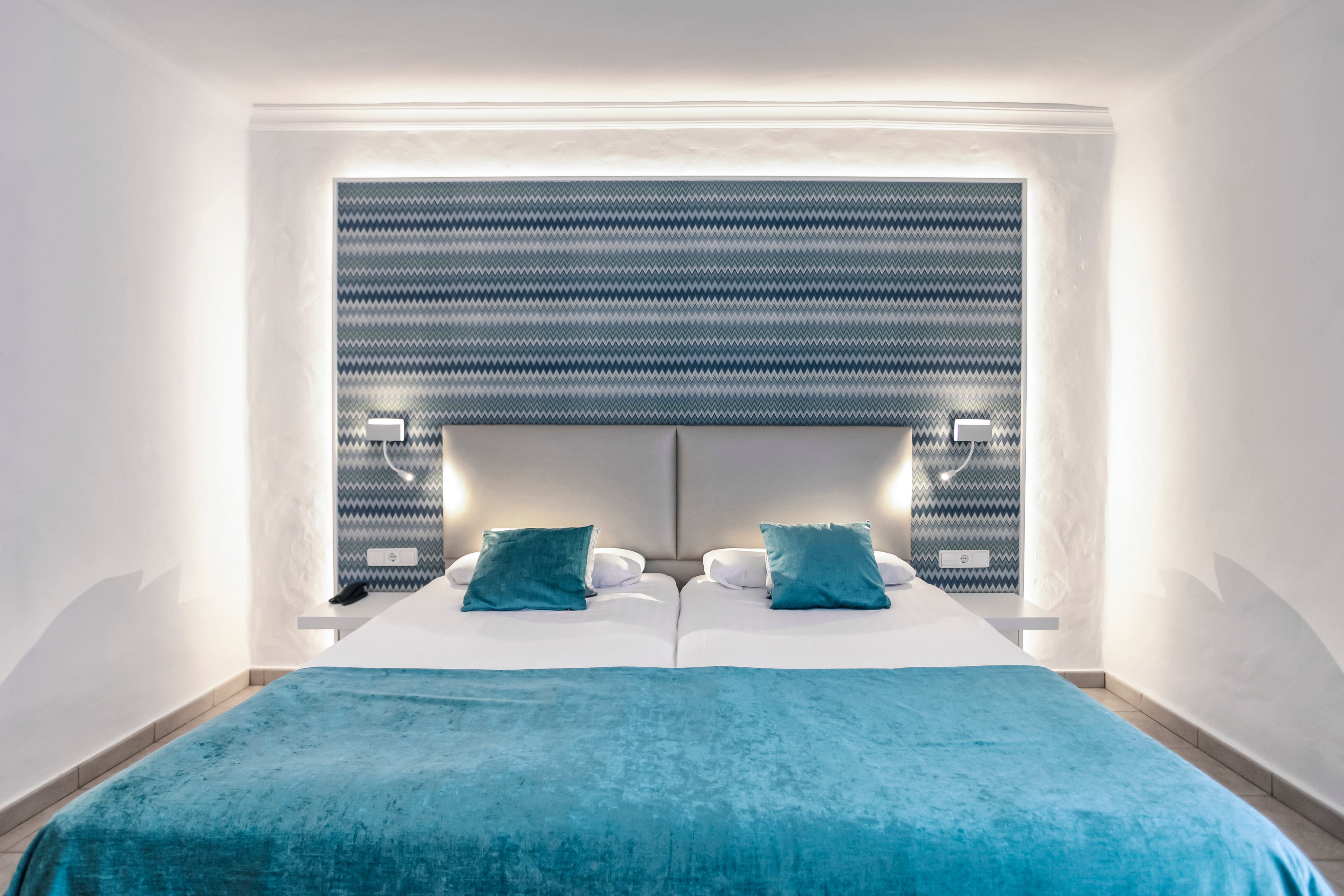 Schlafzimmer mit weißem Bett, blauen Kissen und stilvollem Kopfteil in einem Aldiana Club