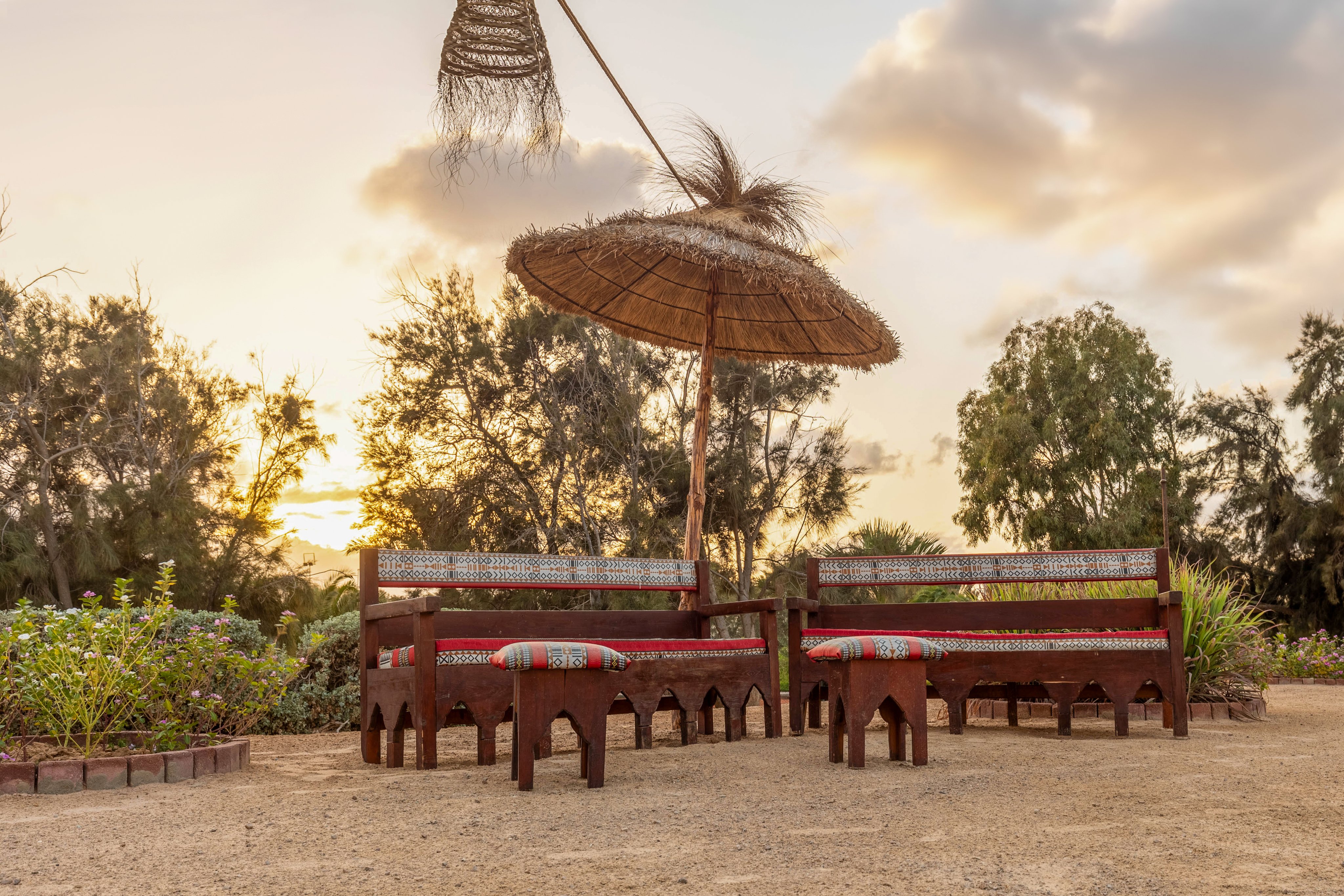 Drei gemütliche Sitzbänke mit Sonnenschirm auf einem Hotelgelände bei Sonnenuntergang