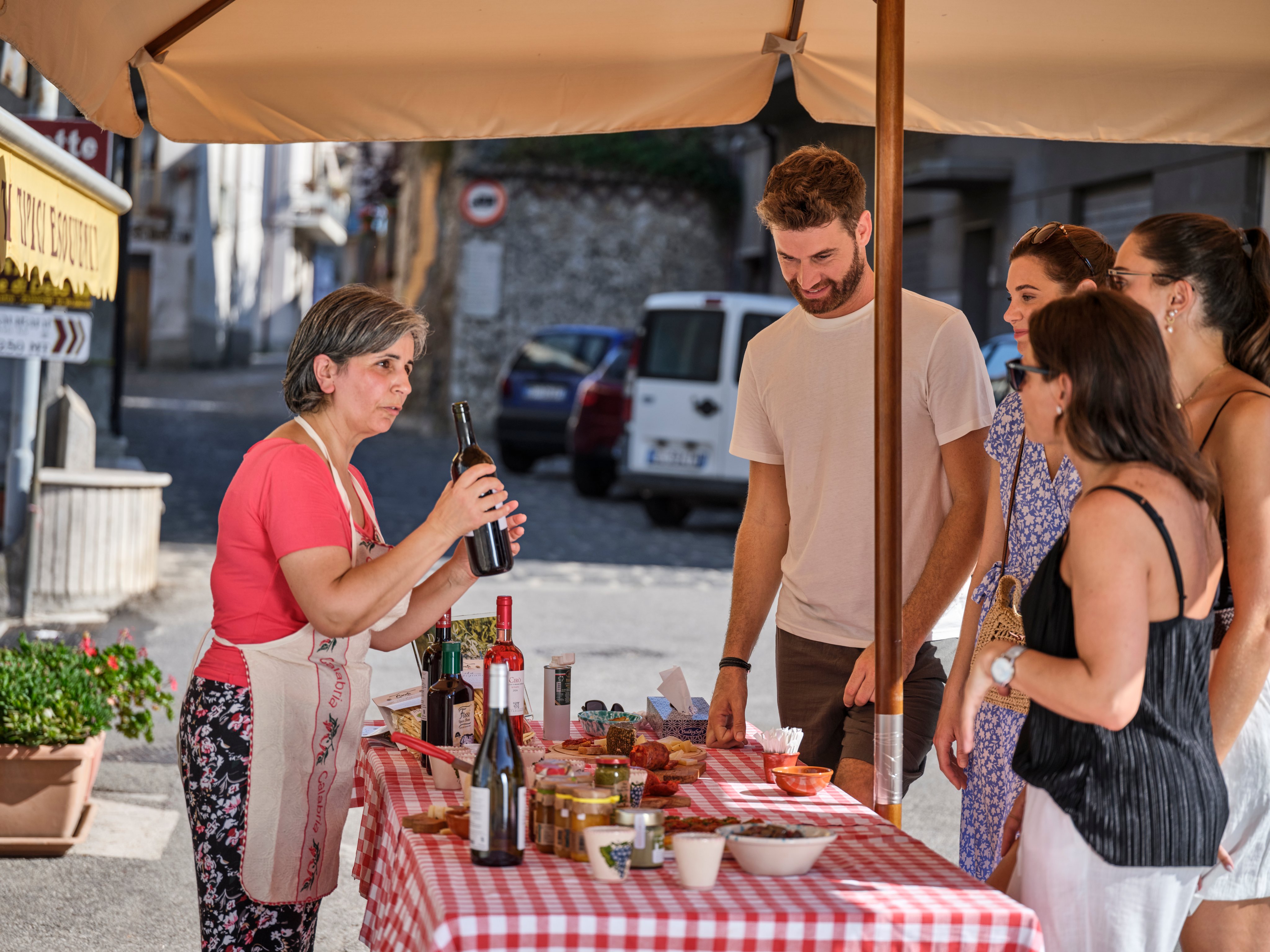 Menschen beim Basar an einem Sonnentag, unter Sonnenschirm, mit Weinen und Produkten auf einem Tisch