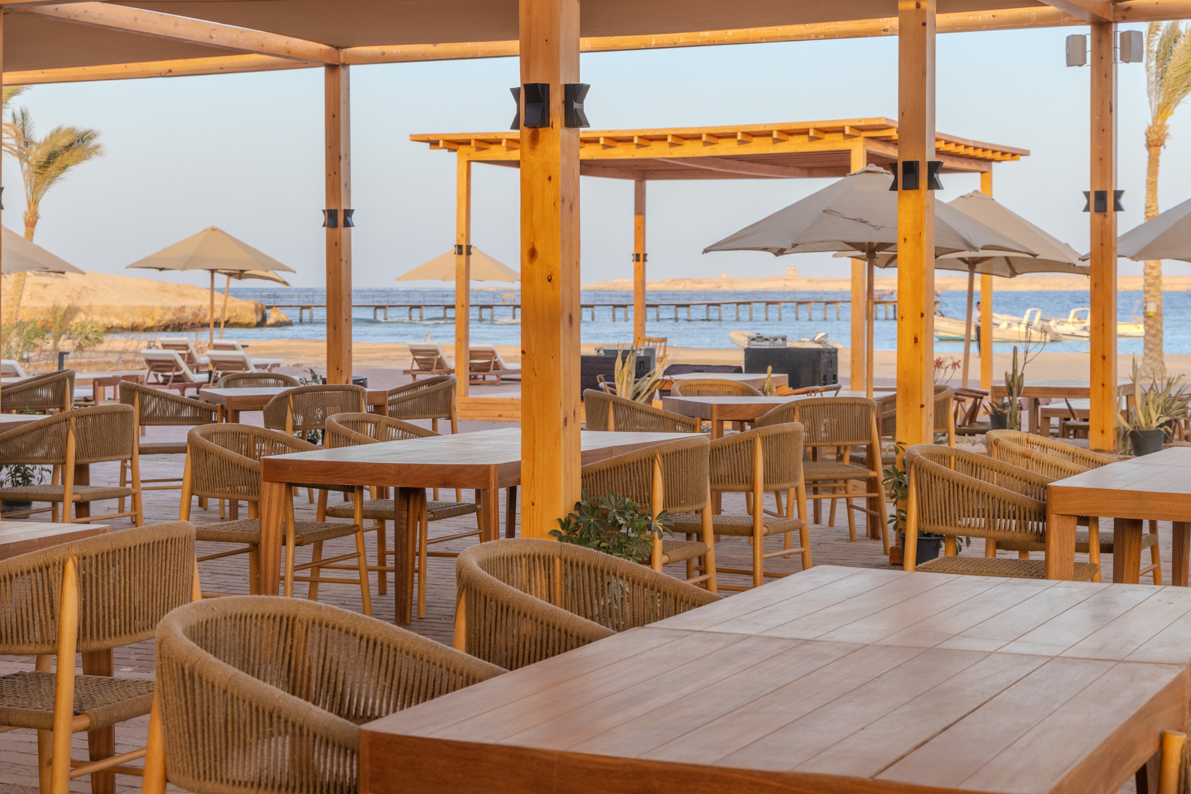 Ein leerer Strandrestaurantbereich mit Tischen, Stühlen und Sonnenschirmen im Freien.
