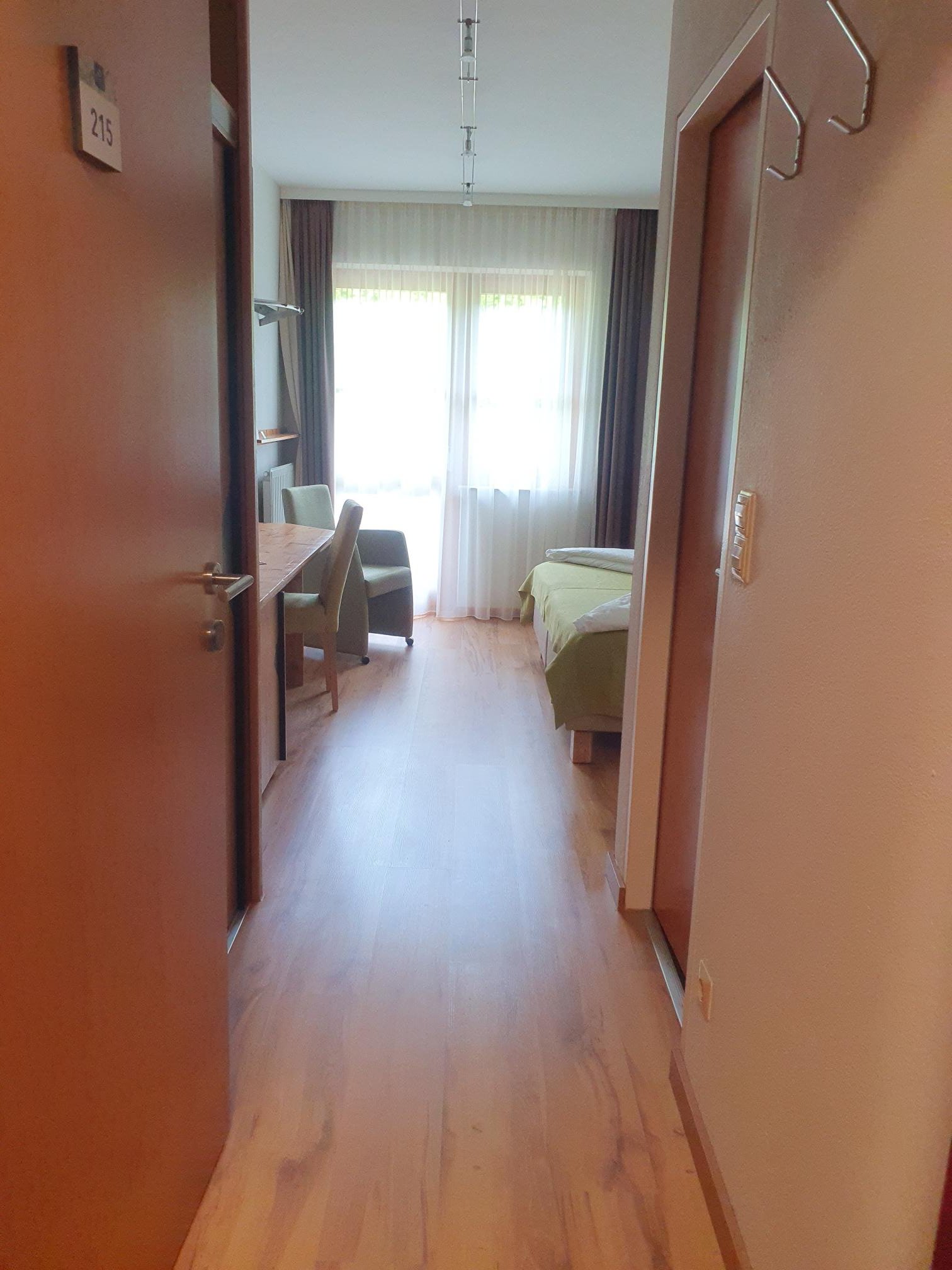 Helles Hotelzimmer mit Bett, Arbeitstisch und große Fenster mit Vorhängen
