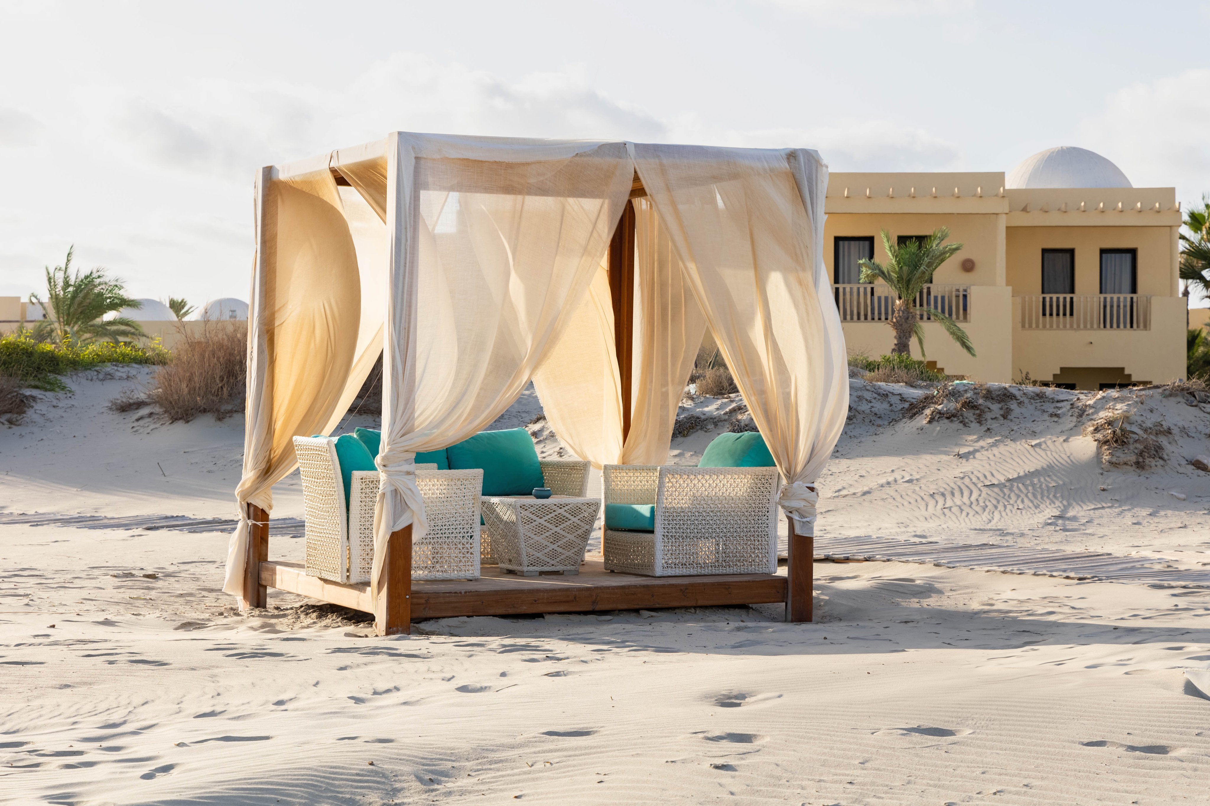 Elegante Strandlaube mit Blick auf Sandstrand und Hotel im Hintergrund, ideal für Premium Urlaub