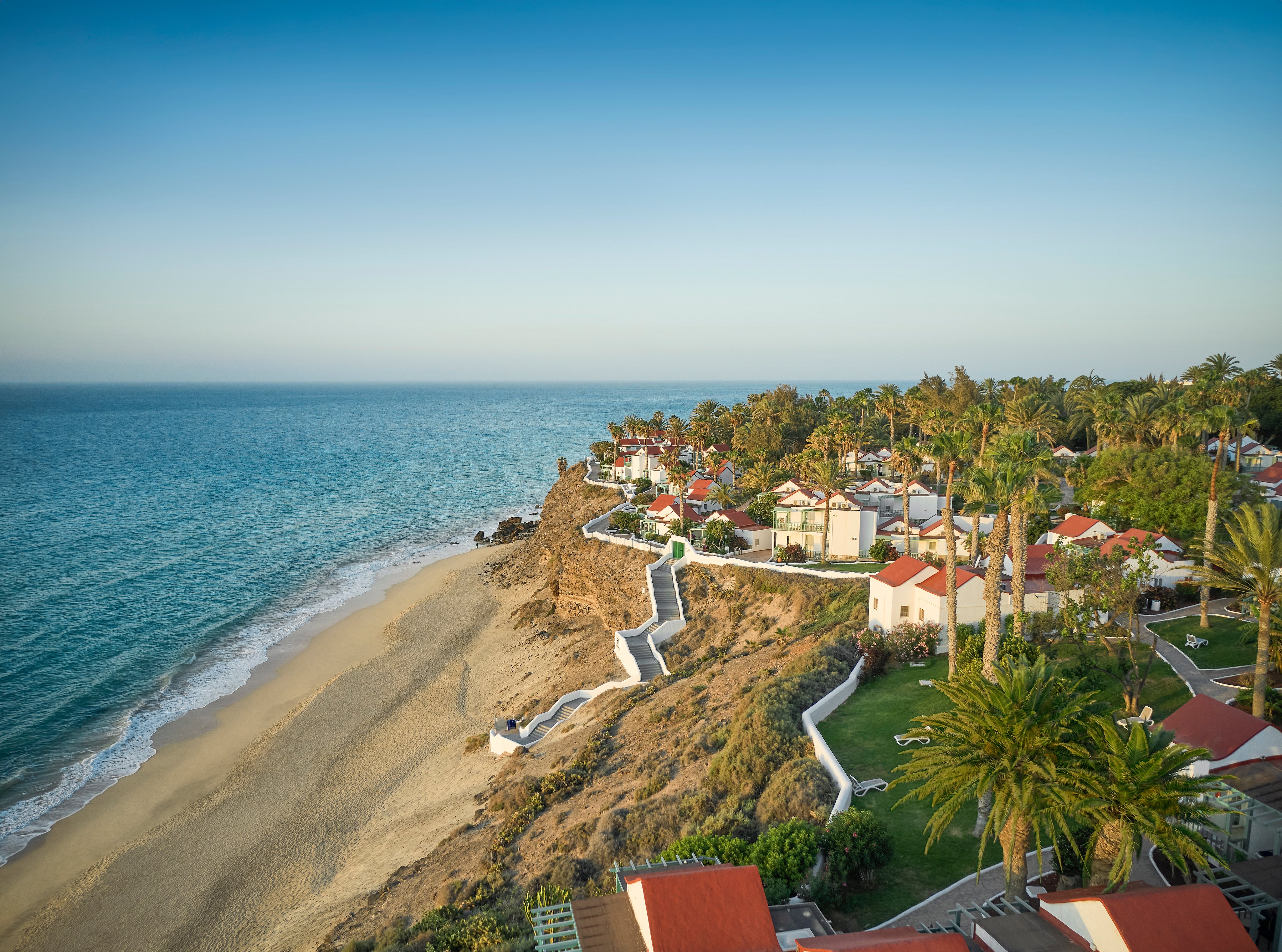 Blick auf eine luxeriöse alldiana Clubanlage am Strand mit Palmen und Meer, Premiumurlaub