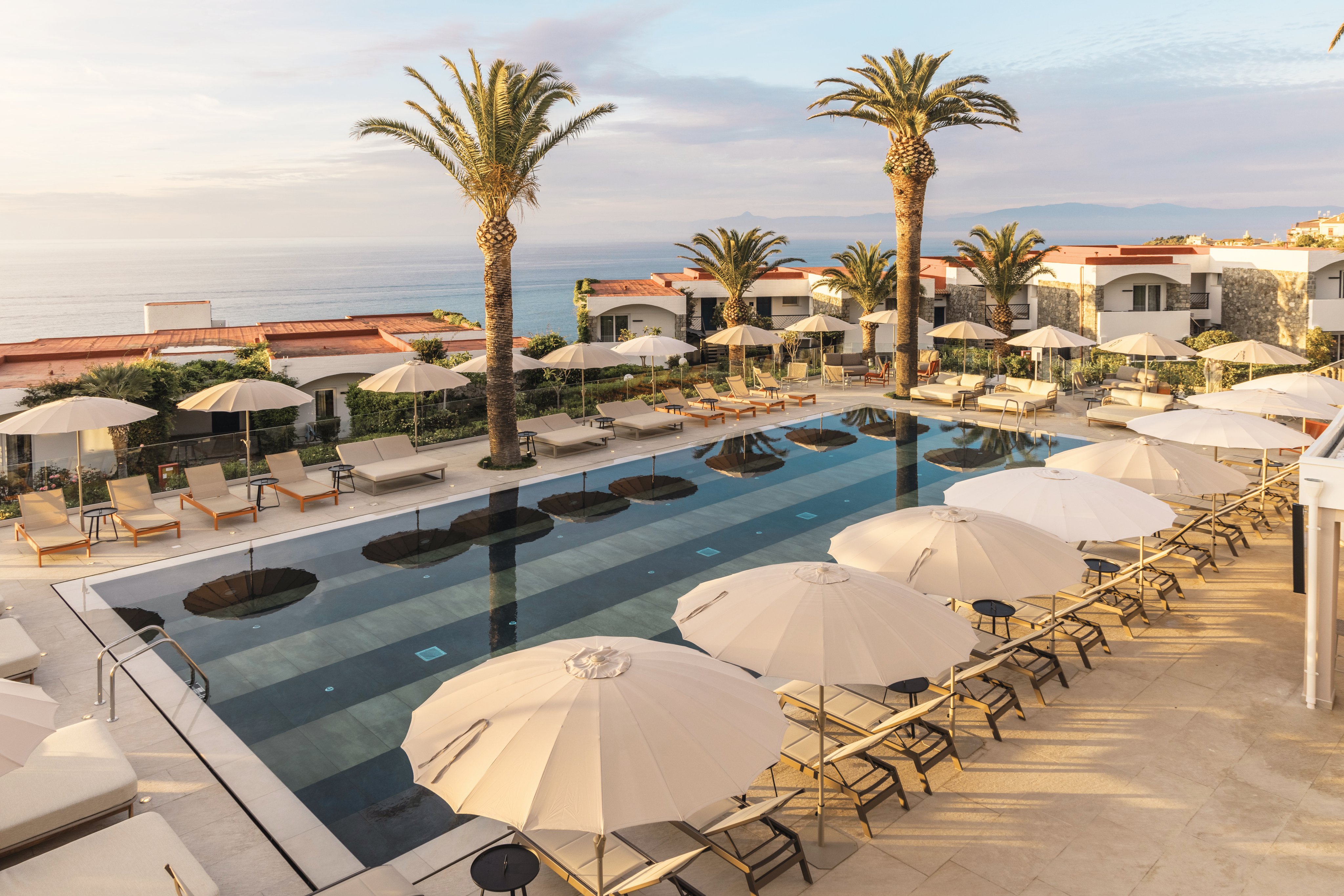 Badebereich mit Pool, Palmen, Liegestühlen und Sonnenschirmen am Meer bei Aldiana