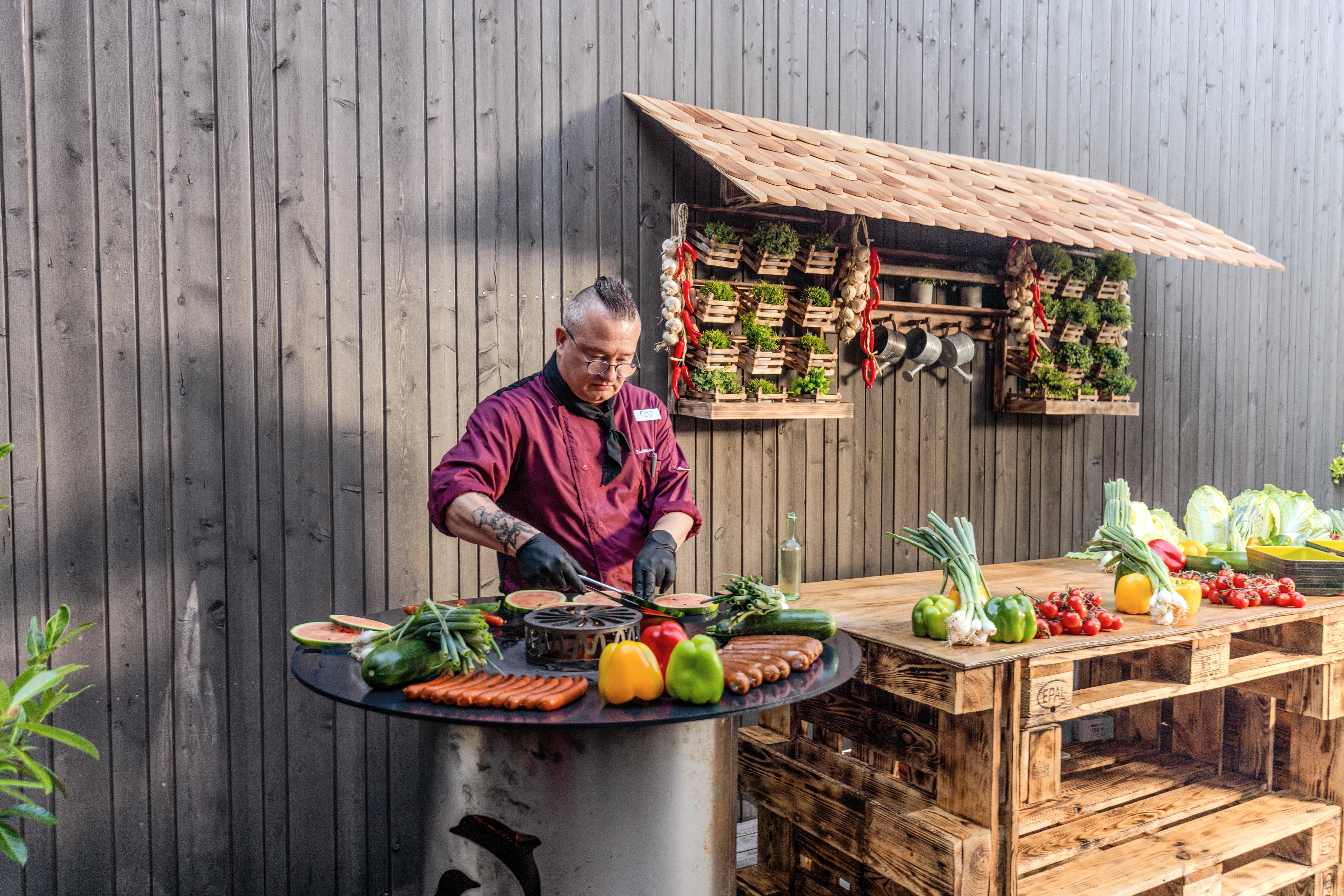 Person beim Grillen mit frischen regionalen Produkten vor einer Holzfassade