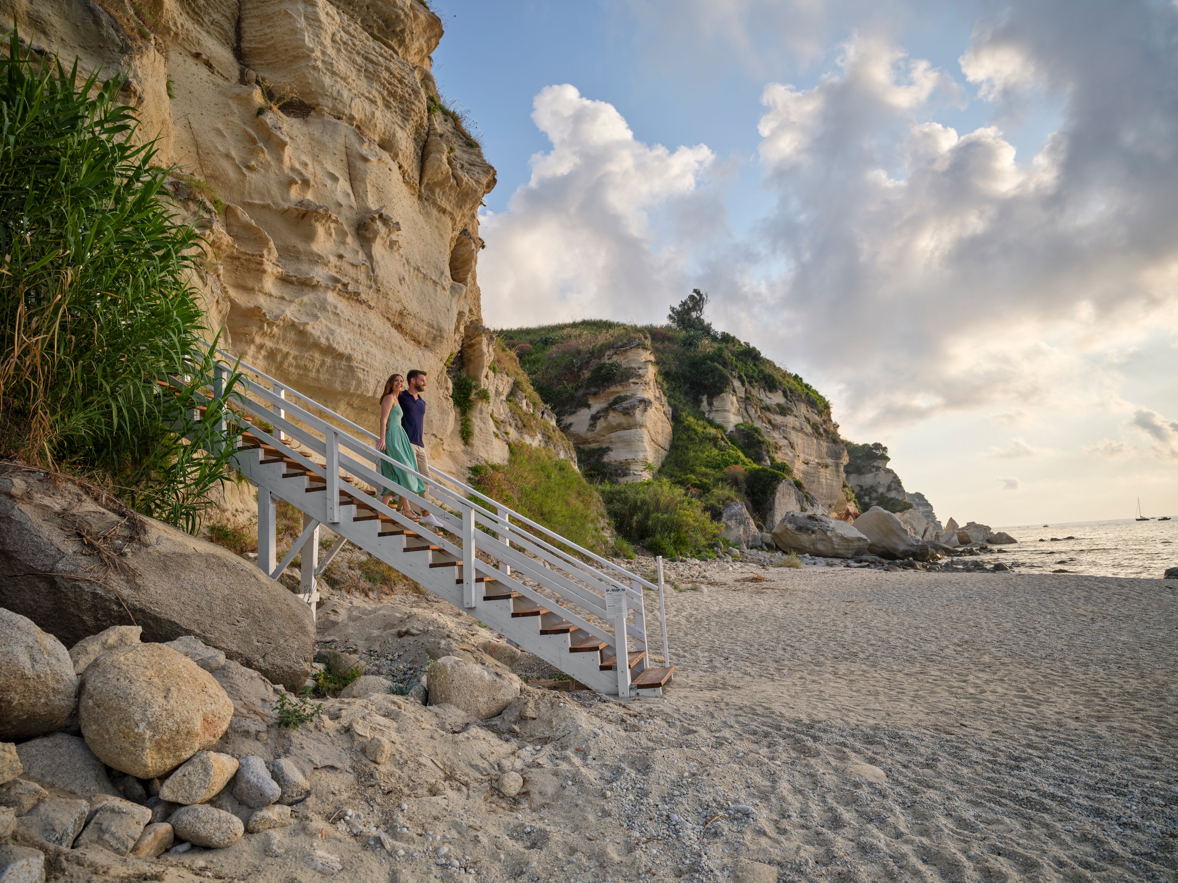 Ein Pärchen geht die Treppe zum Strand bei Sonnenuntergang an der Küste entlang