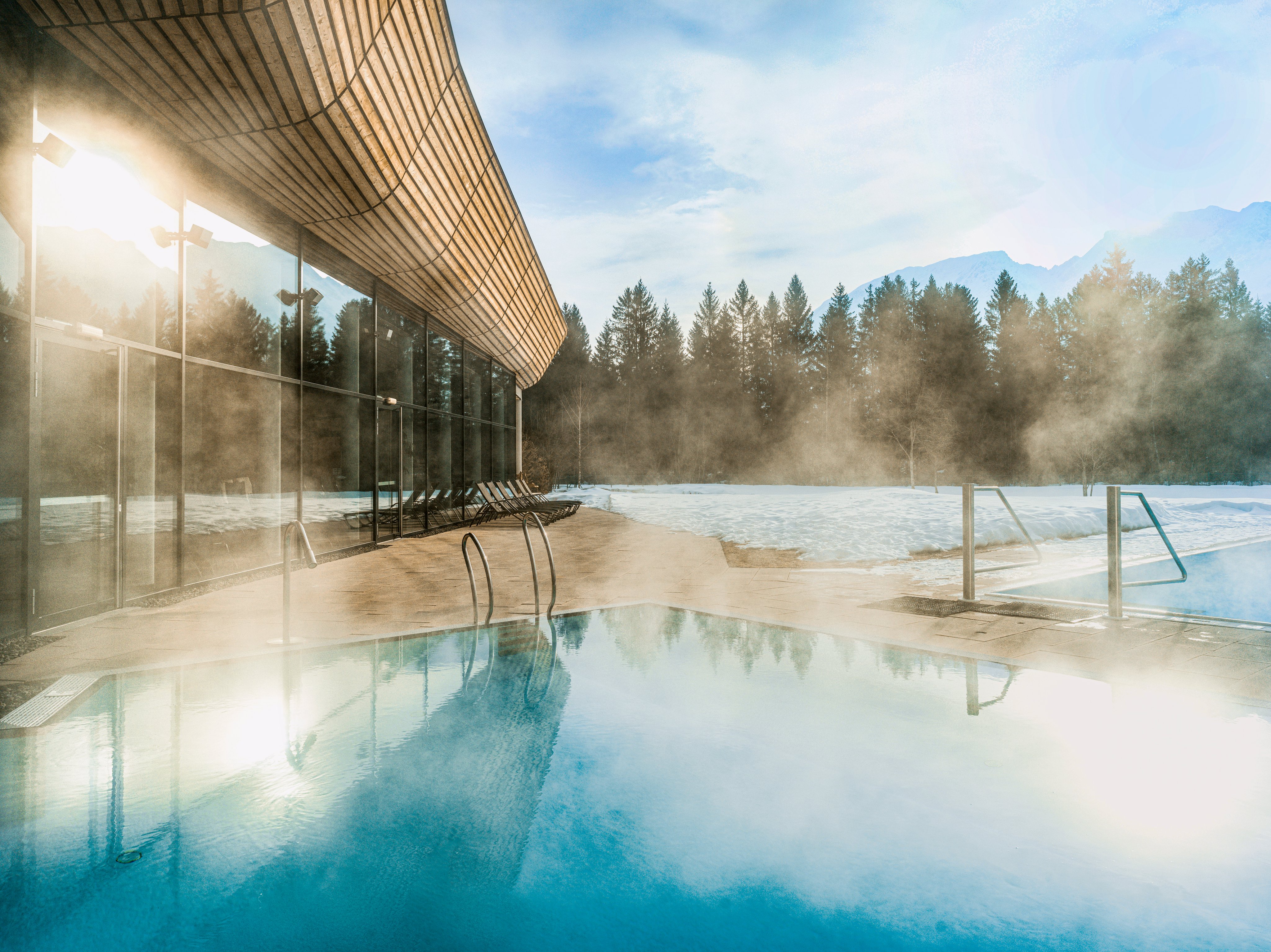 Ein Außenpool mit Blick auf Bäume und Berge, Nebel über dem Wassermorgen, modernes Gebäude