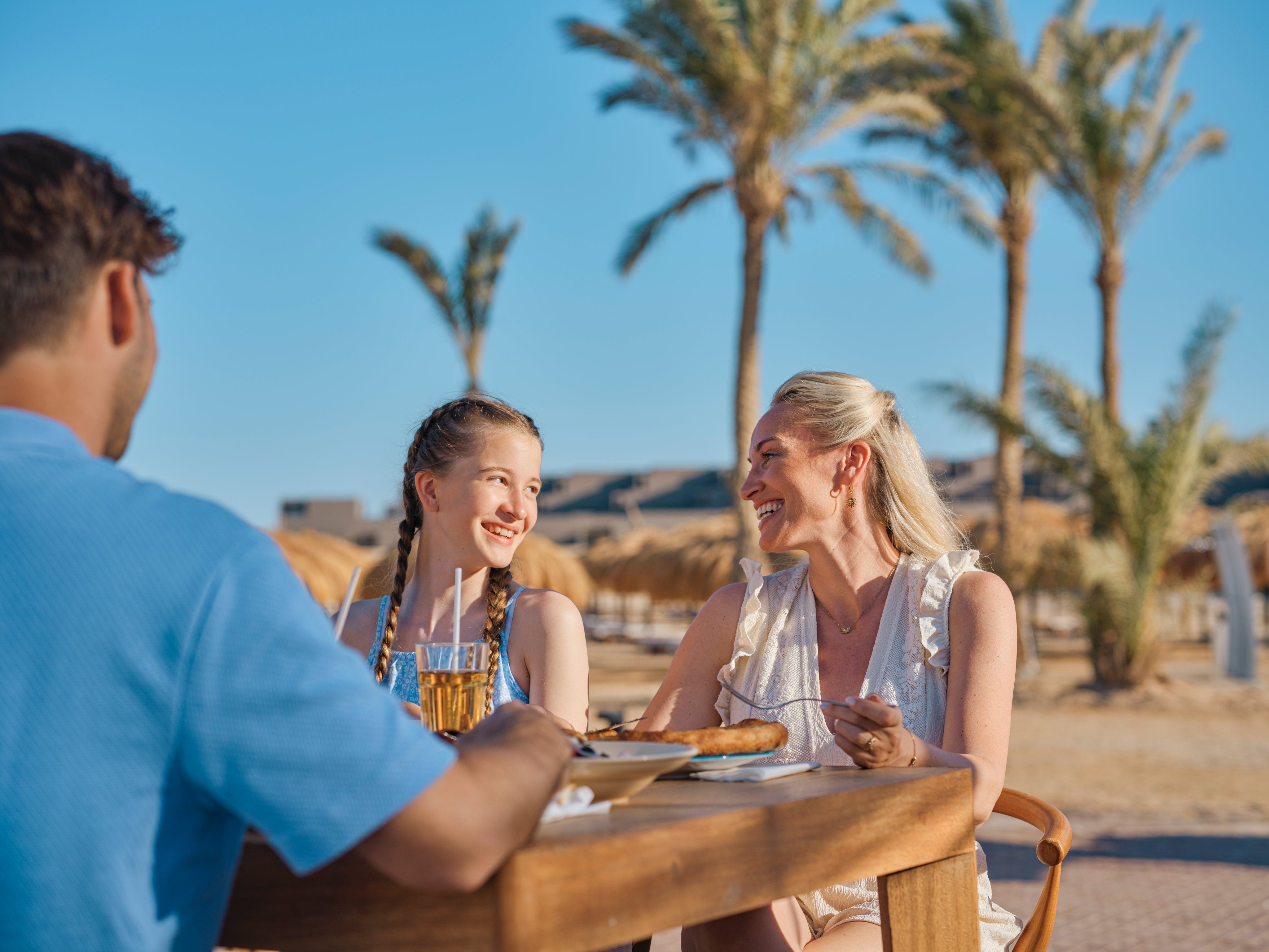 Zwei Frauen und ein Mann essen und trinken am Tisch im Strandurlaub bei Aldiana
